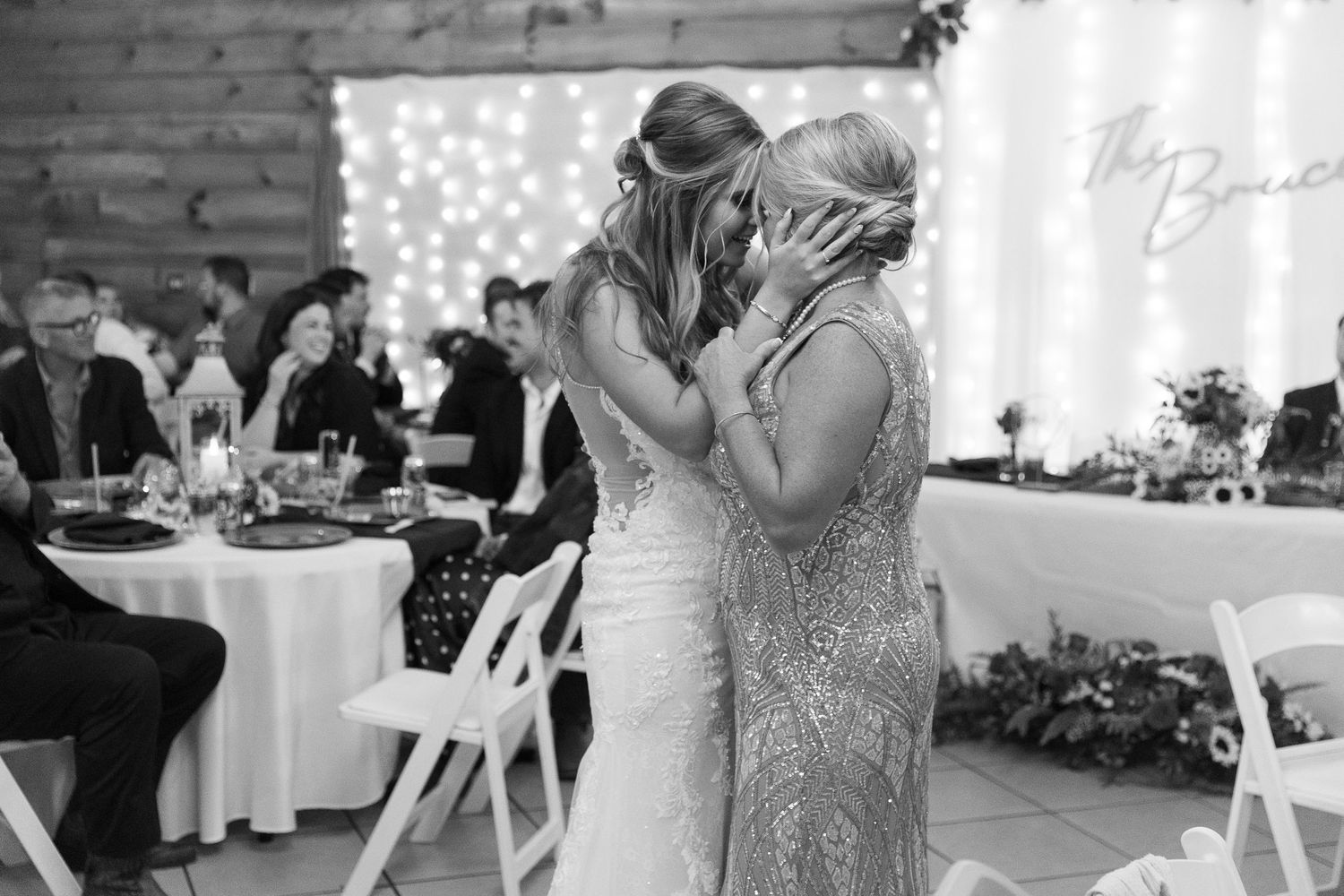 Emotional moment between two guests during wedding reception with twinkle lights in background.