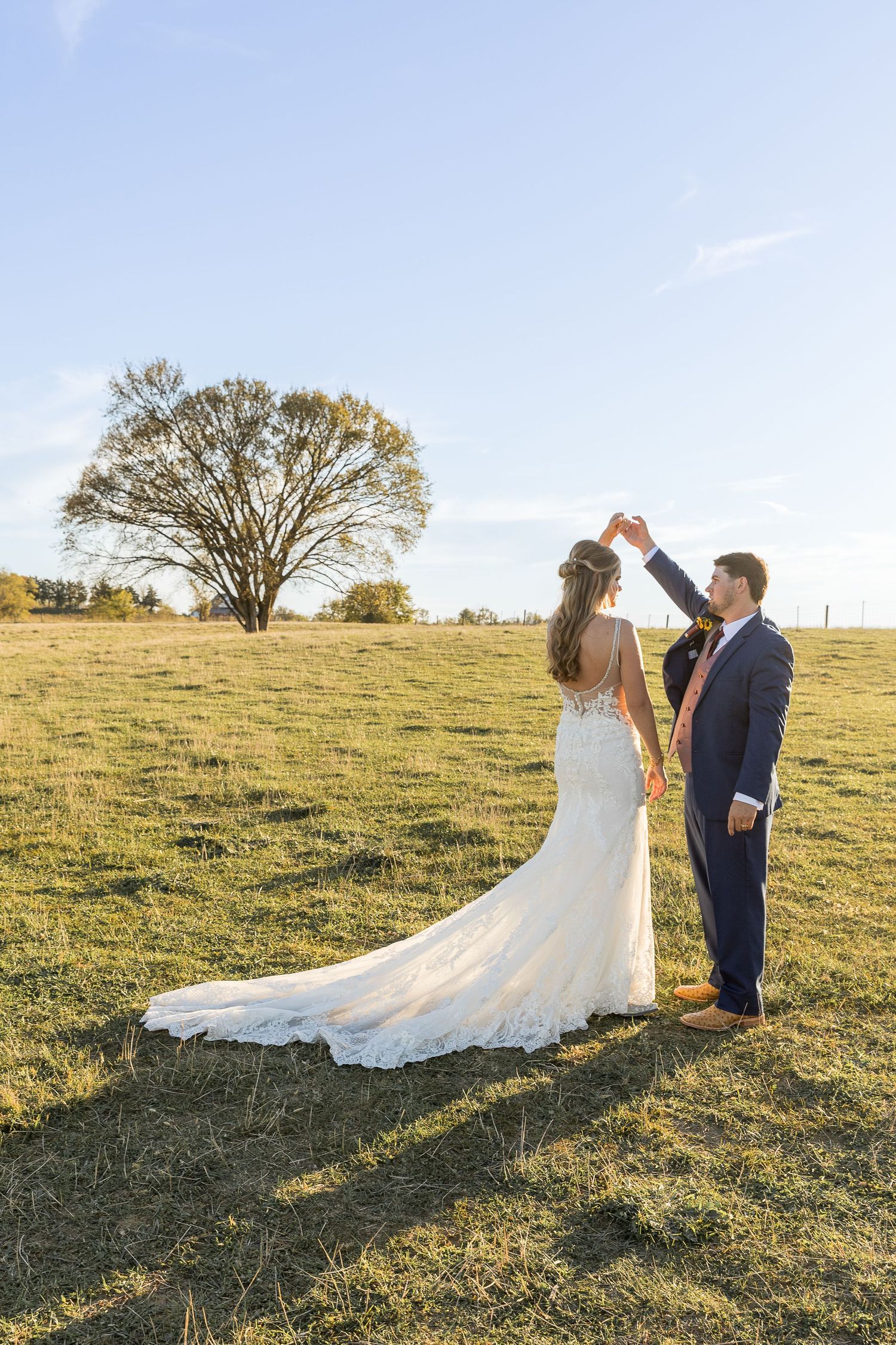 A bride and groom dance in a golden field with a large tree in the background.