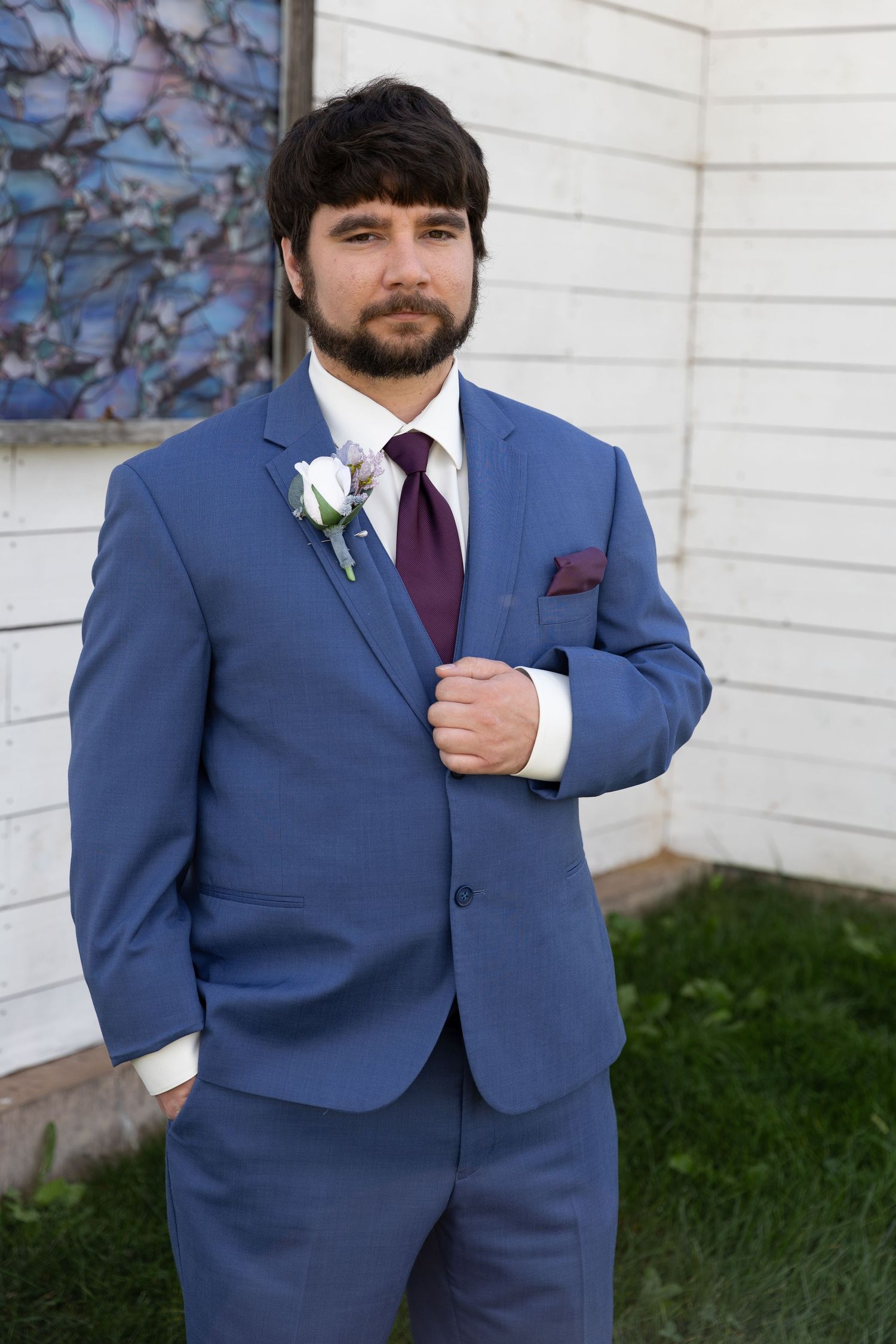 Groom wearing navy blue suit with burgundy tie and white boutonniere.