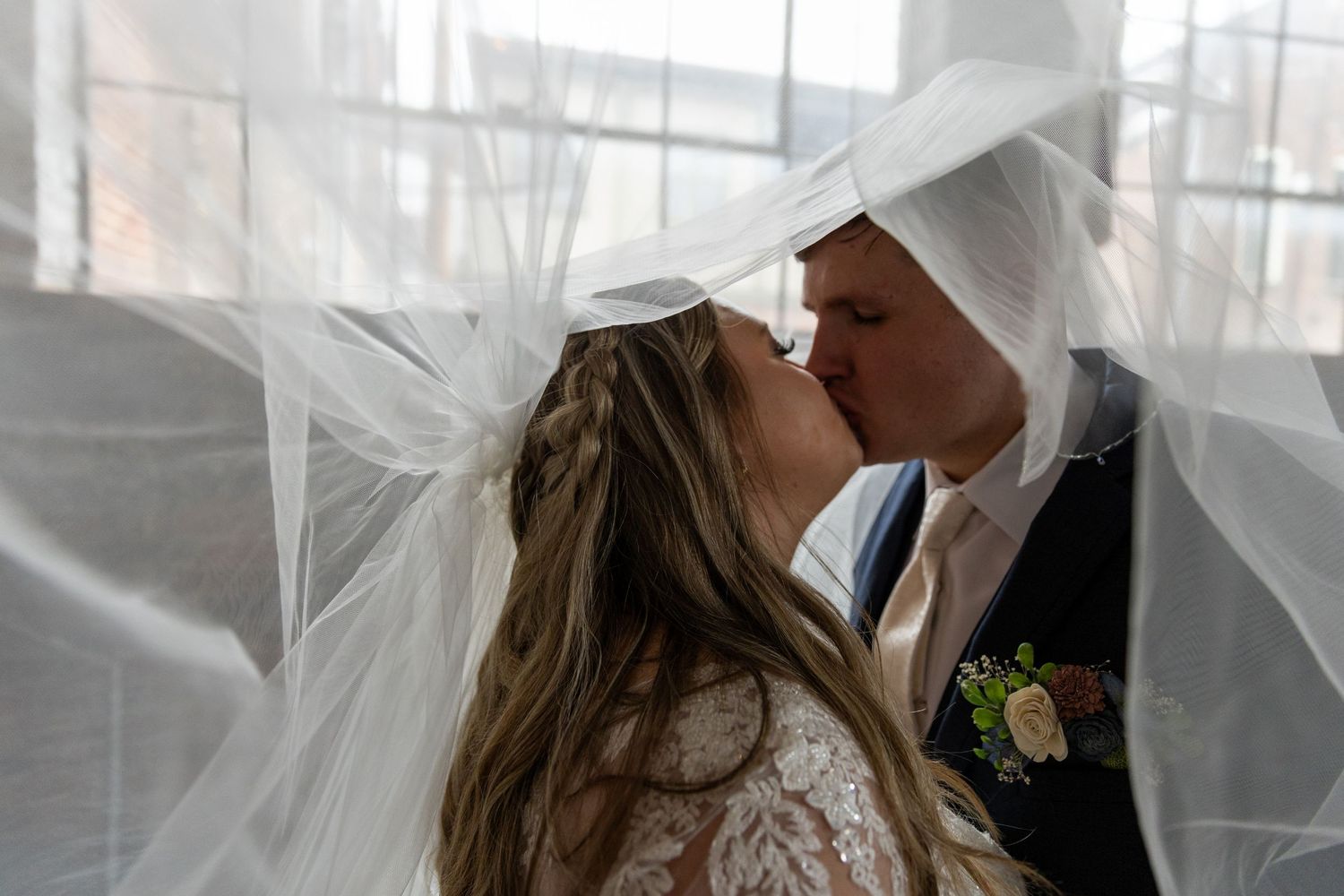 A romantic wedding kiss captured through delicate white veil during an intimate ceremony.