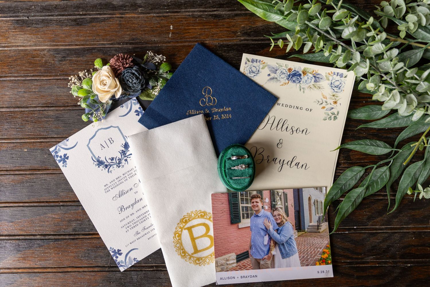 Wedding invitation suite with blue passport, floral details, and decorative stationery on wooden background.