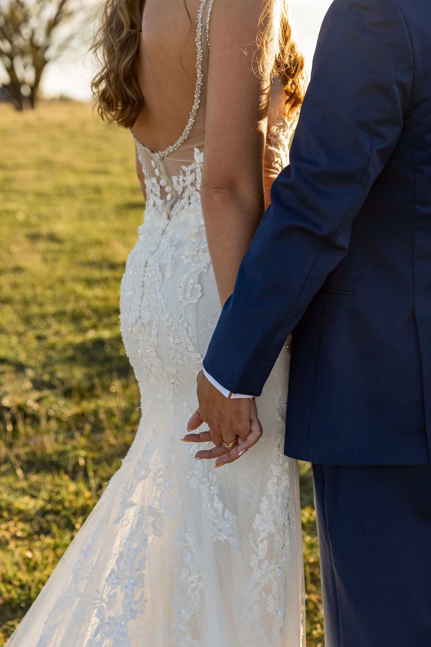 Close-up of bride and groom holding hands, showing detailed lace wedding dress and navy suit.