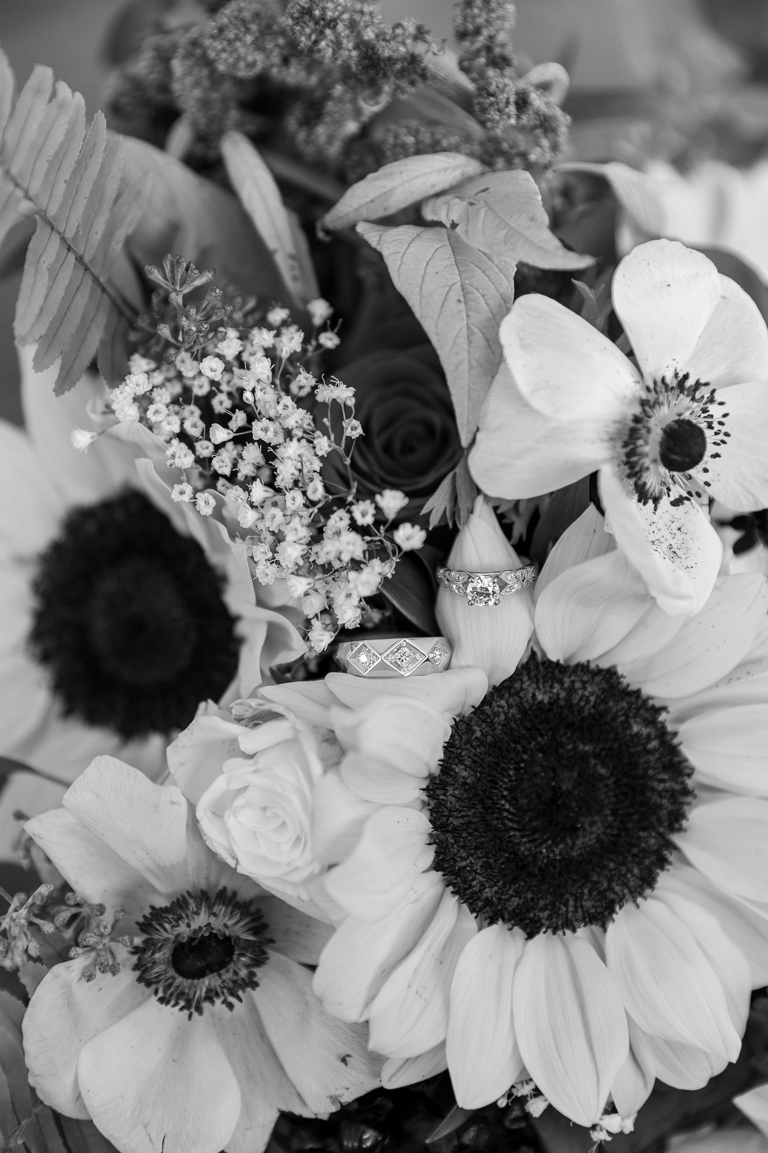 Black and white photo of wedding rings nestled among sunflowers and delicate florals.