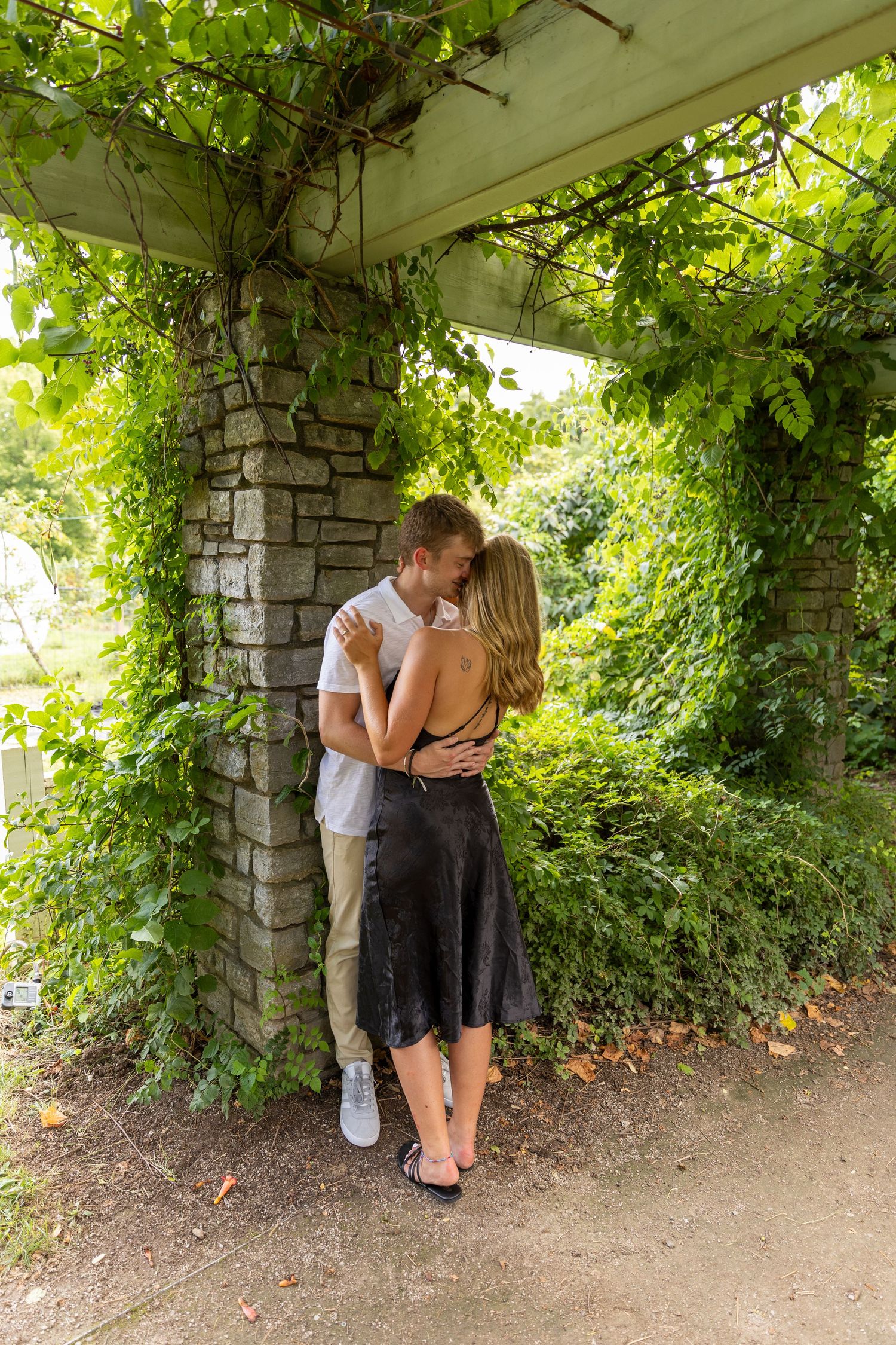 Romantic moment captured under an ivy-covered stone archway in a garden setting.