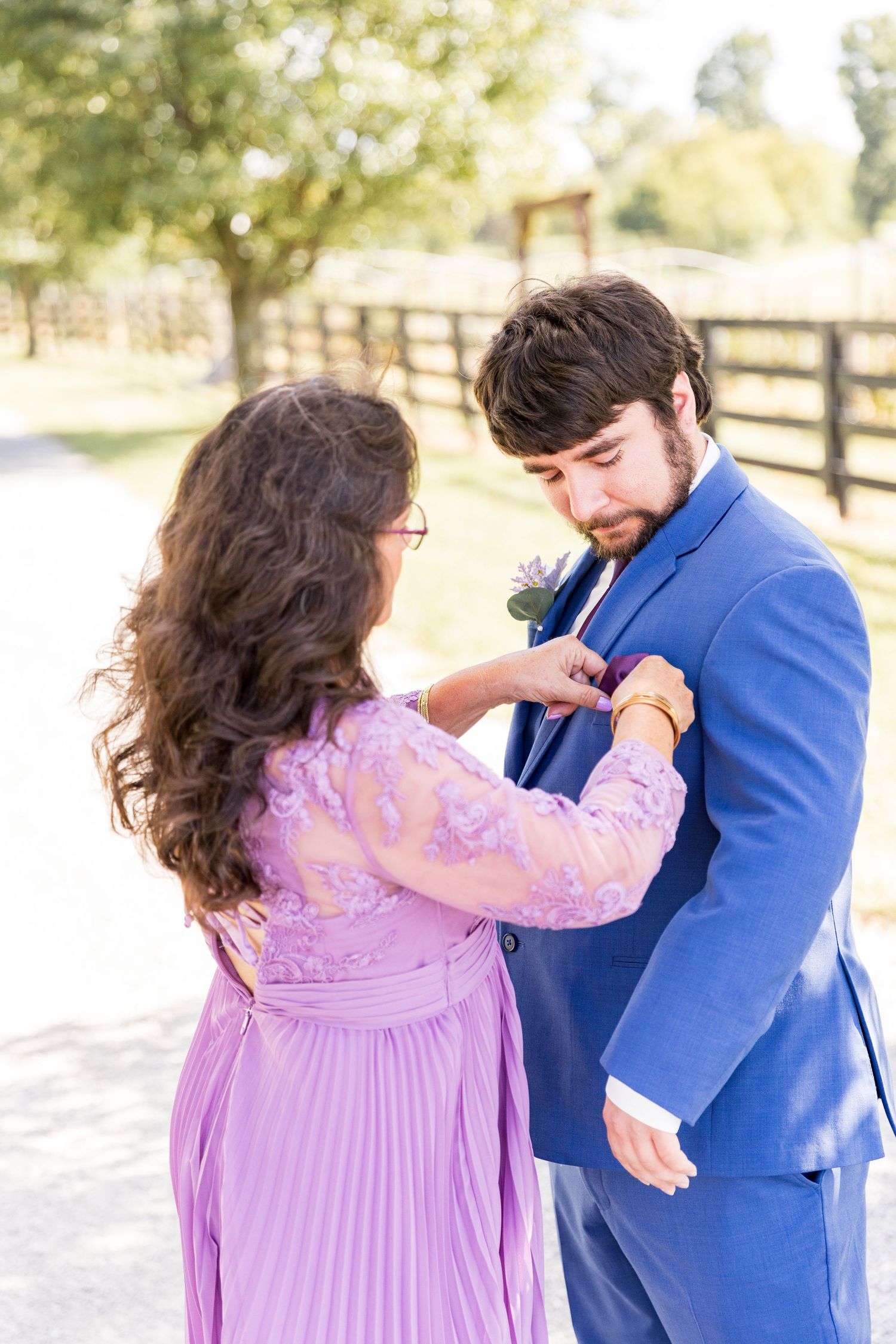 A couple in blue and purple formal attire share a tender moment on a country path.