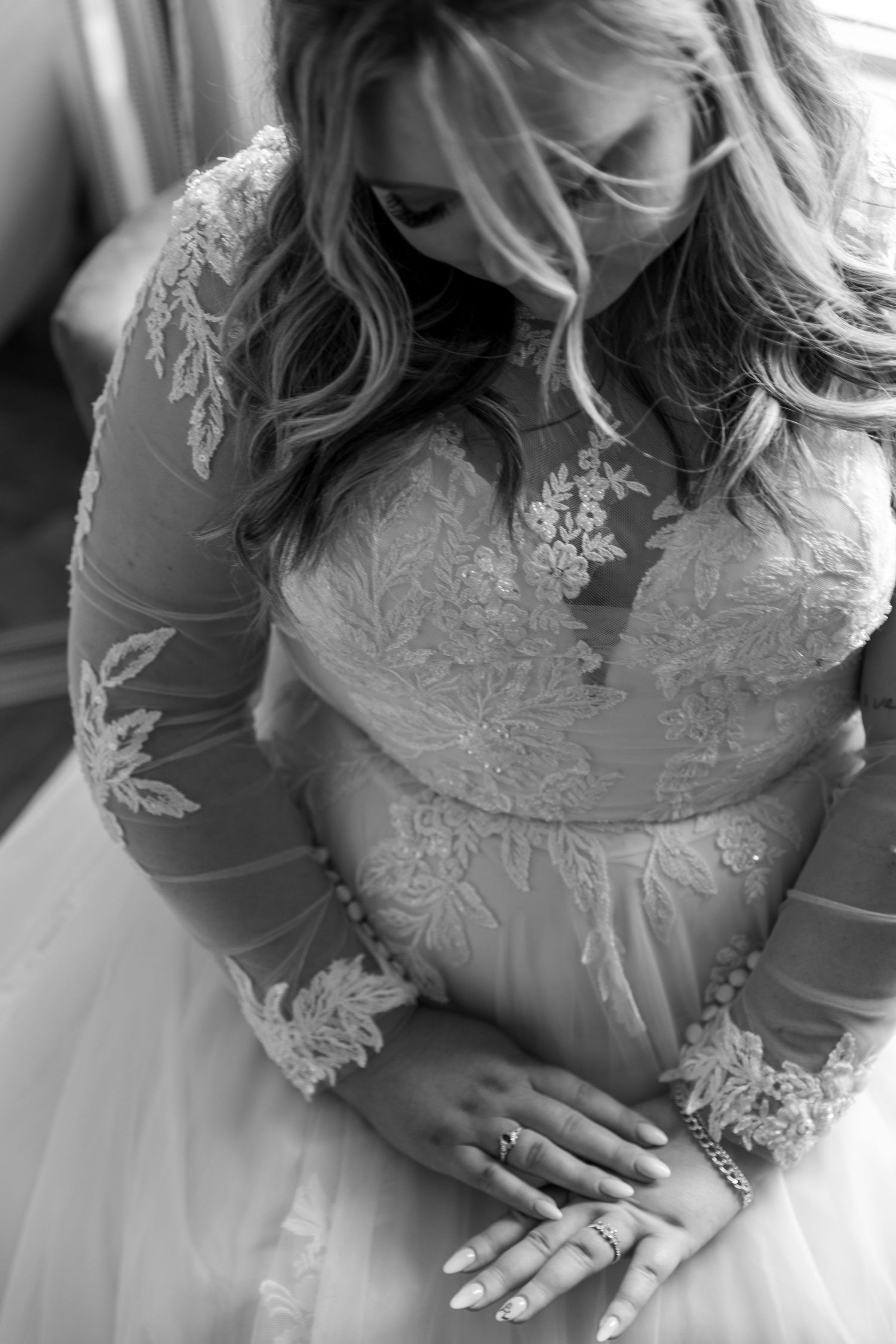 Romantic black and white detail of lace wedding dress with long sleeves and engagement ring.