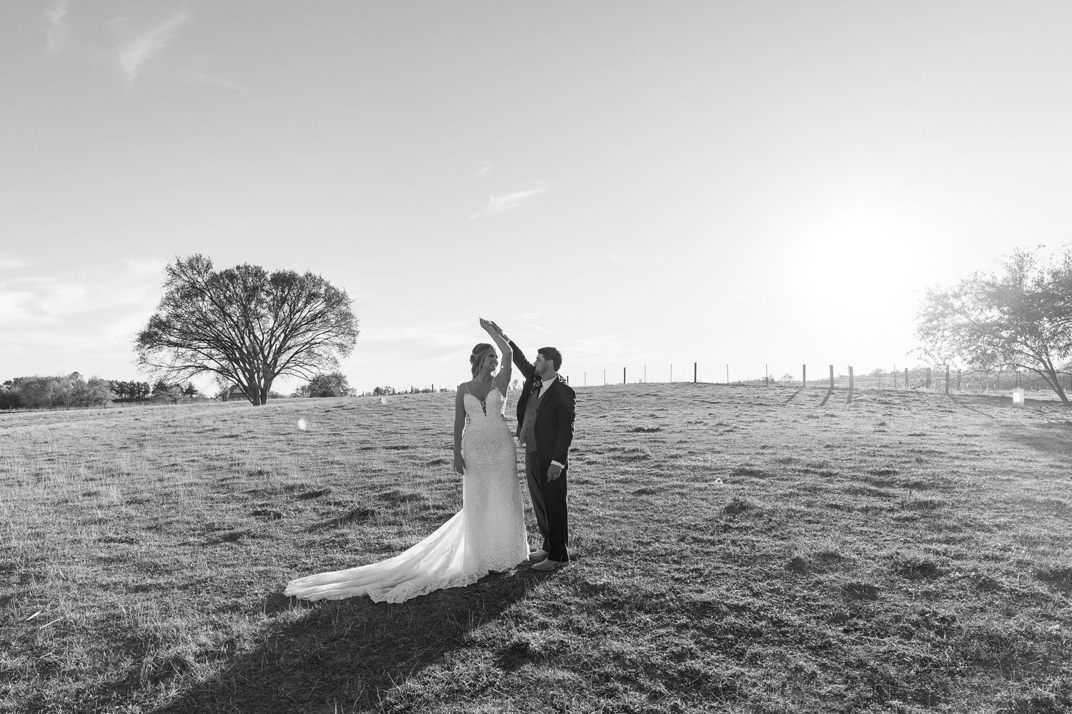 A black and white silhouette of newlyweds standing on a hilltop against the sky.