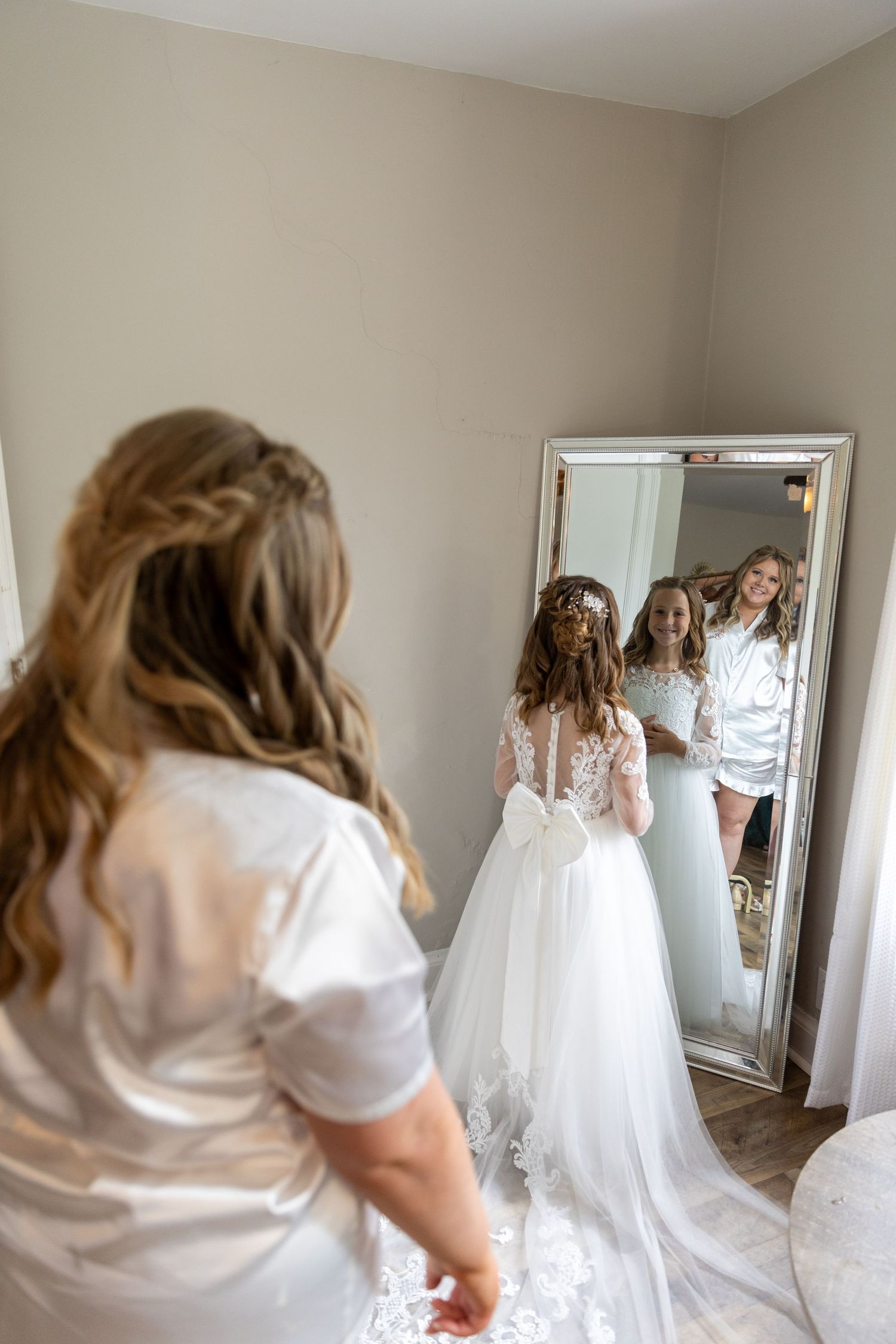 A wedding dress being fitted and admired in a full-length mirror during pre-ceremony preparations.