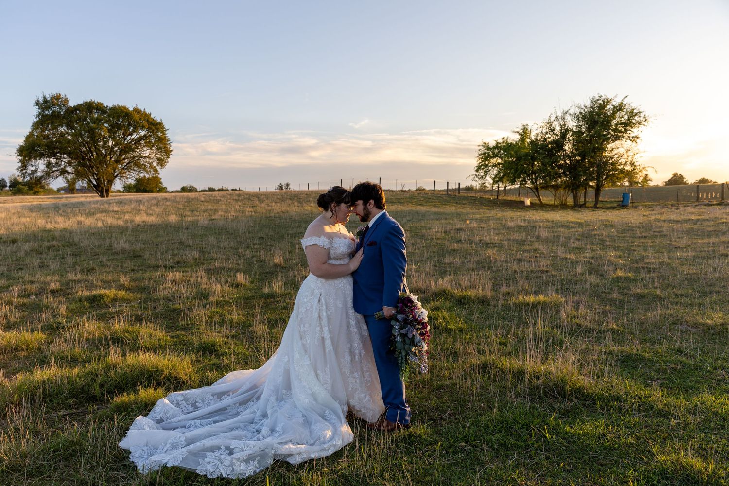 A couple shares an intimate moment in a field during golden hour on their wedding day.