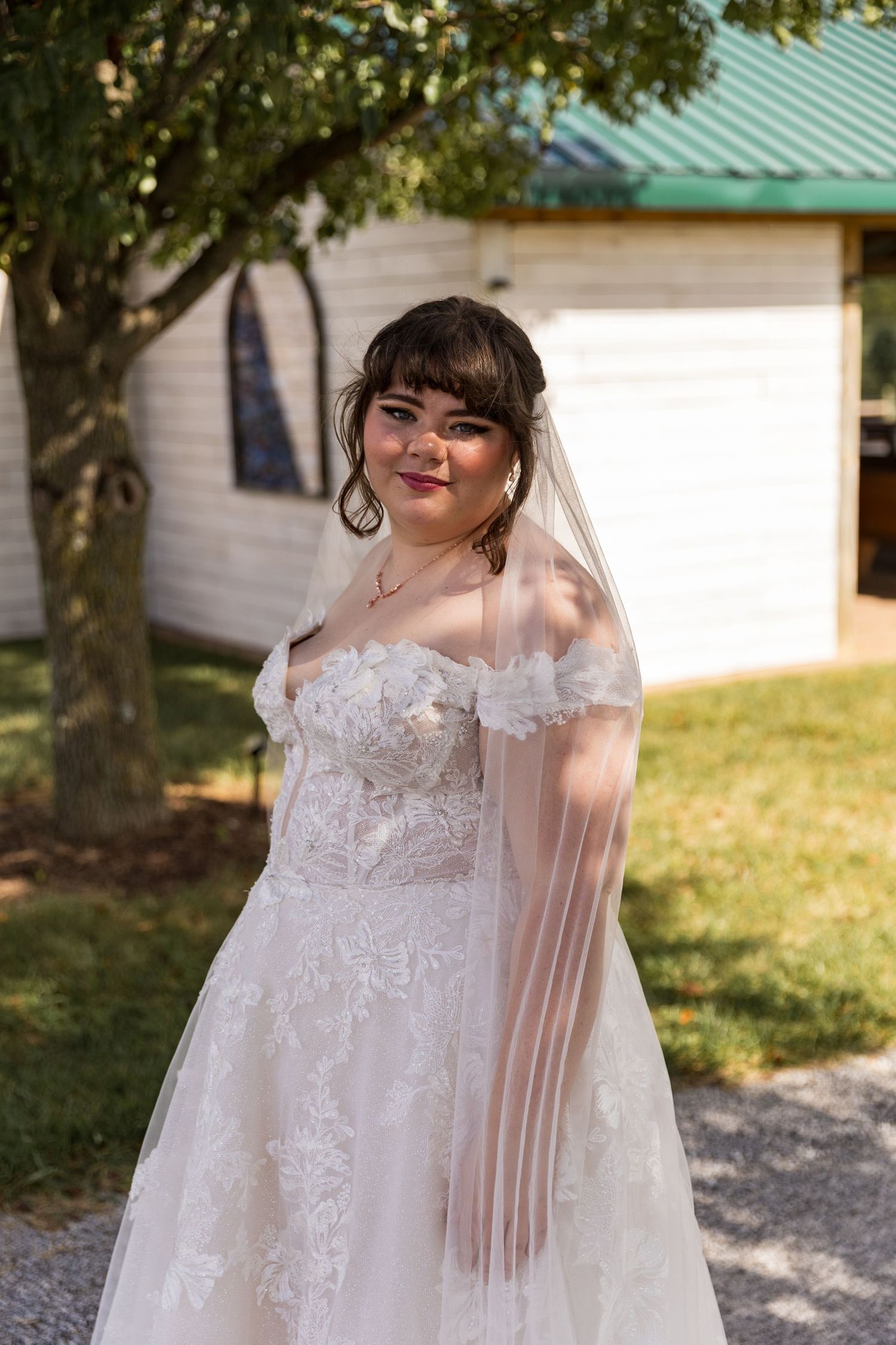 A delicate white lace wedding gown with floral details and sheer sleeves in outdoor sunlight.
