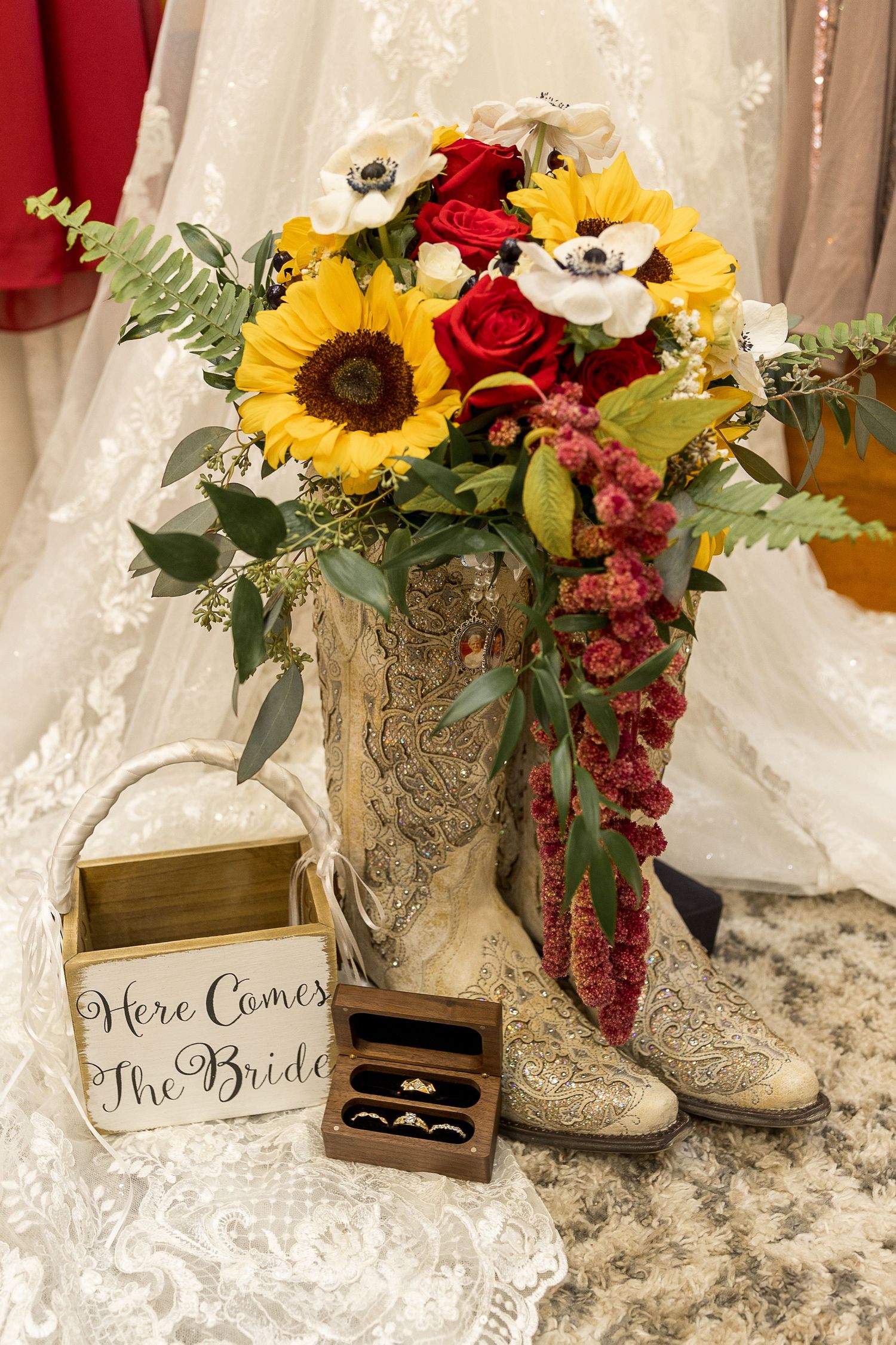 Wedding bouquet with sunflowers and roses in cowboy boots beside 'Here Comes the Bride' sign.