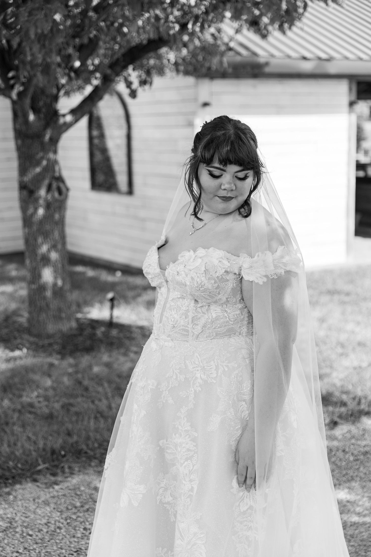 Black and white portrait of bride in lace wedding dress with flowing veil outdoors.