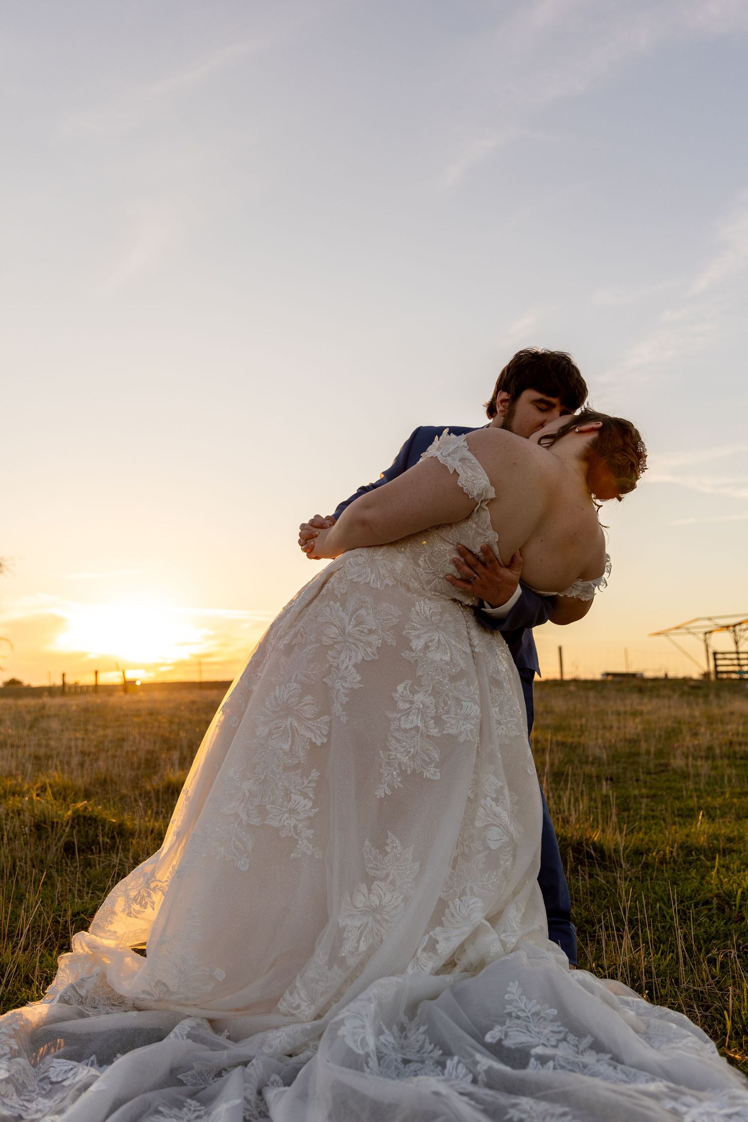 A dramatic sunset silhouettes a couple sharing a romantic dip in their wedding attire.