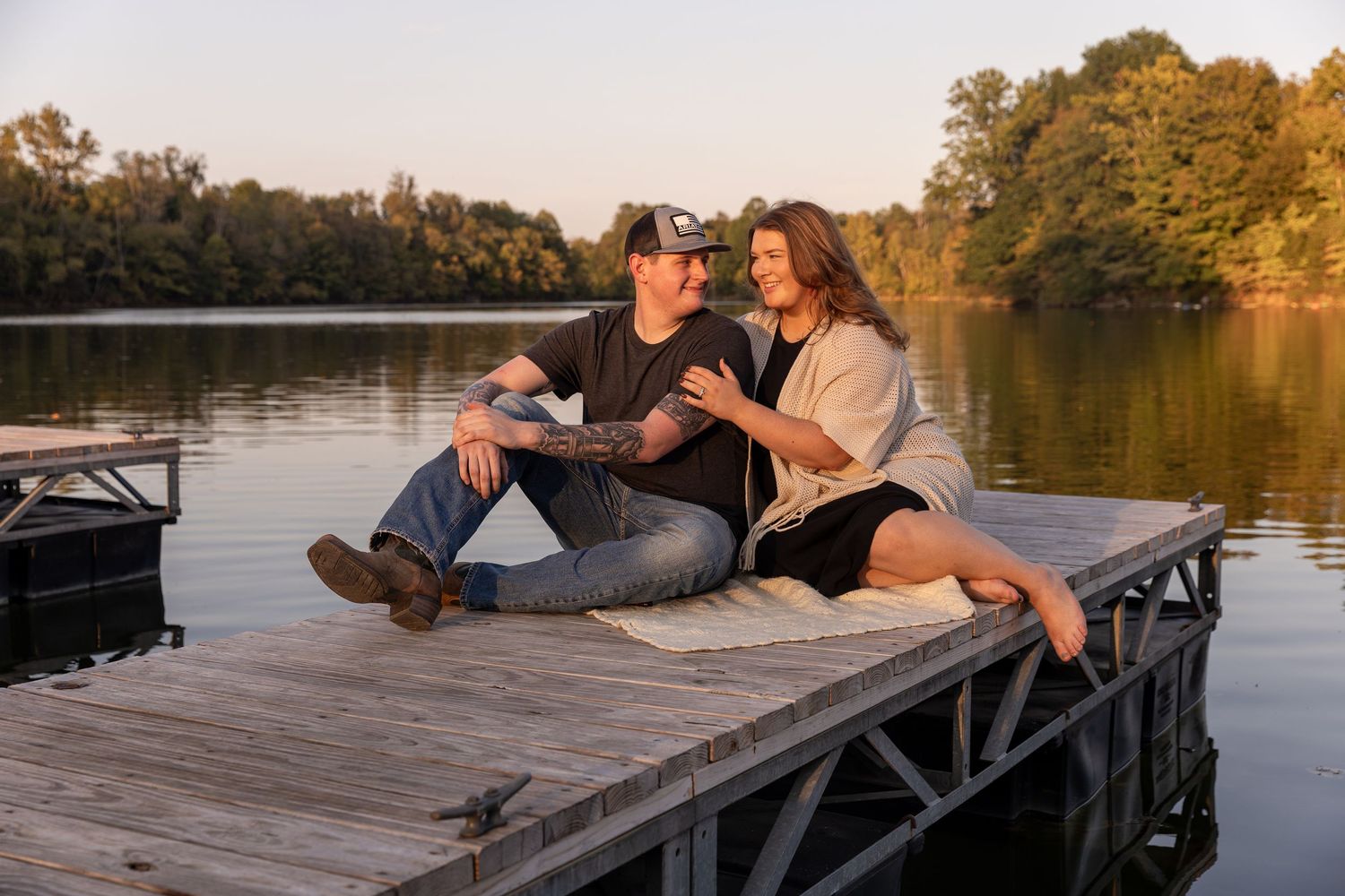 Couple shares intimate sunset moment on wooden dock by tranquil lake during golden hour.