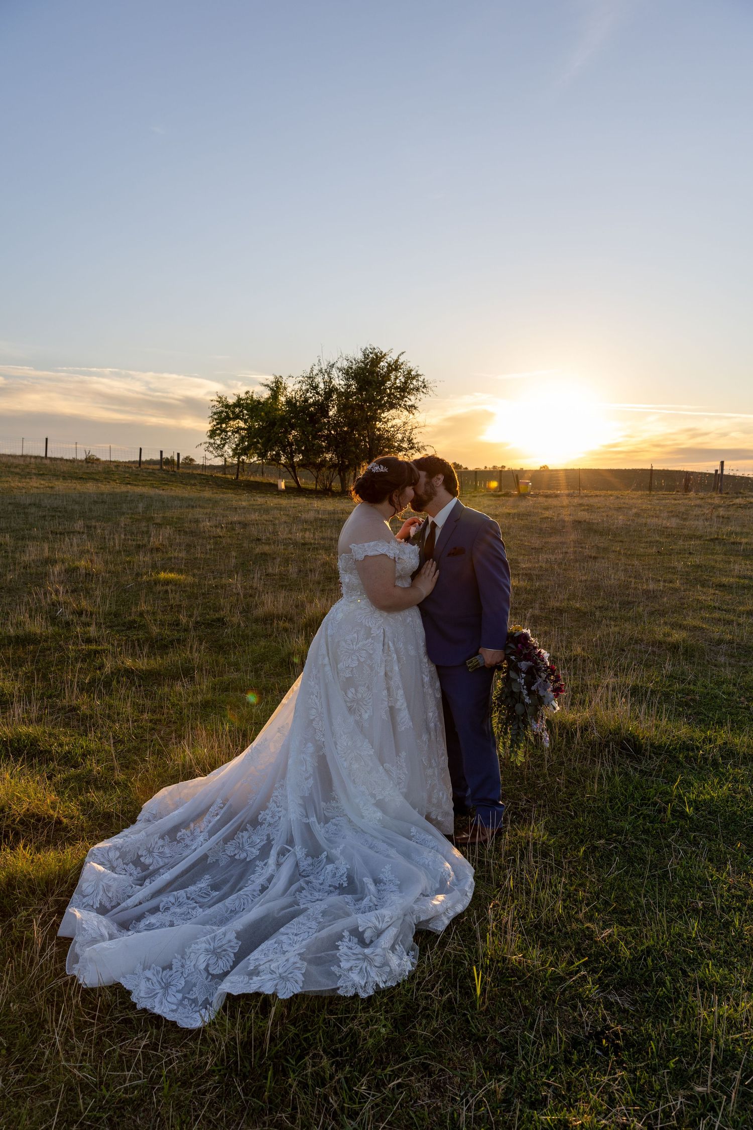 A sunset wedding portrait in a field with a flowing lace dress train.