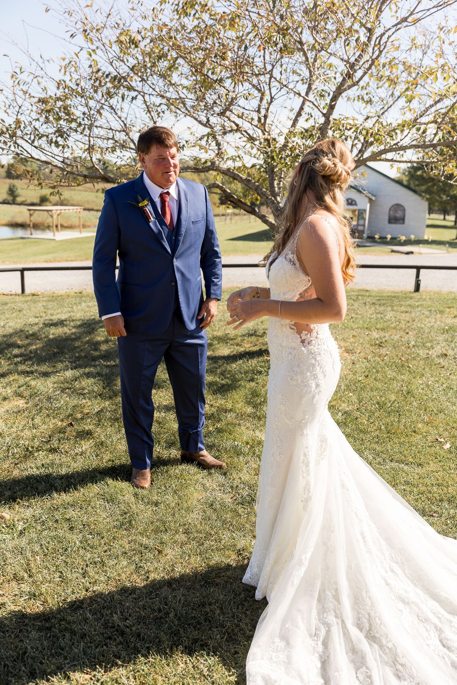 A wedding couple standing on grass with a white chapel visible in the background.