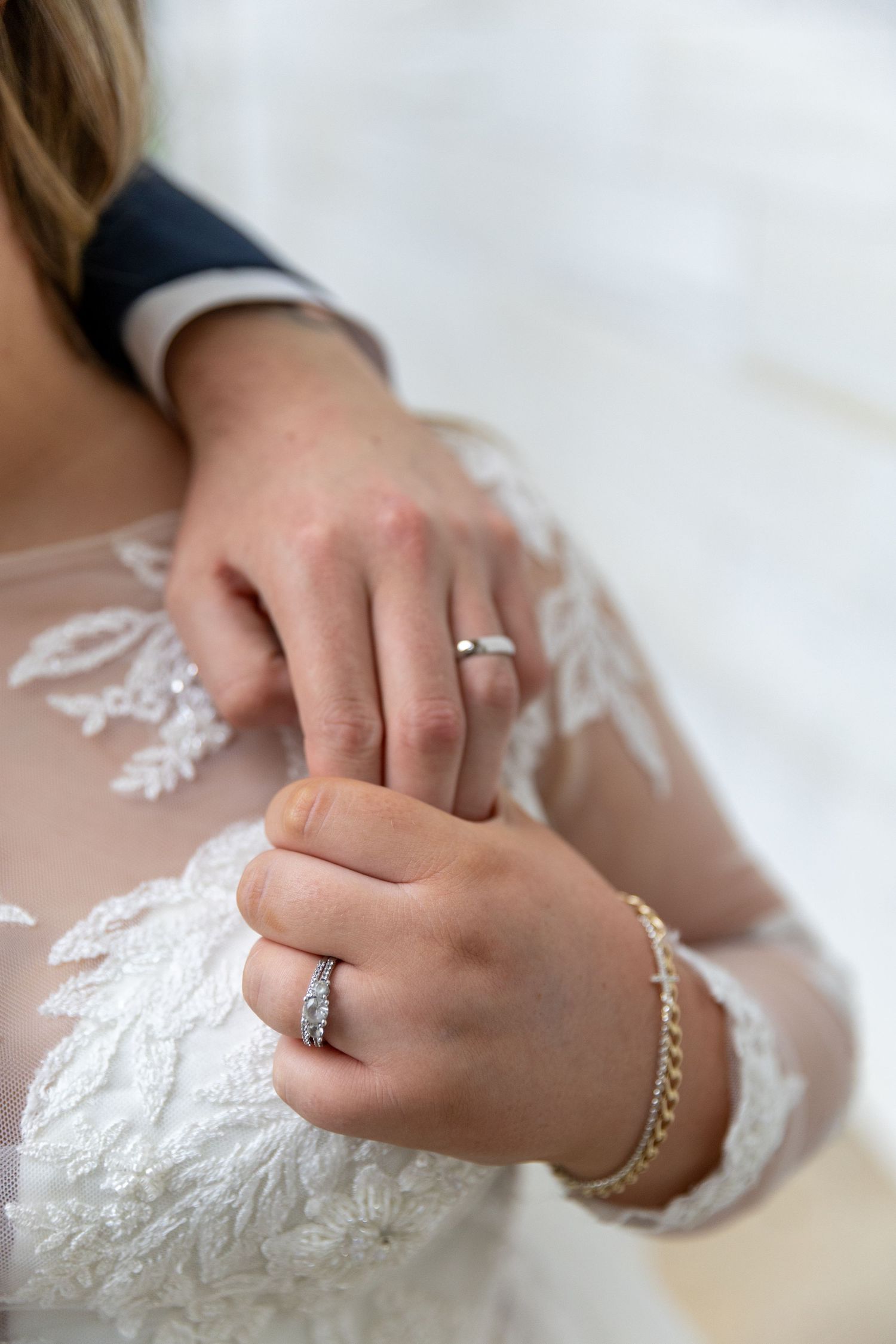 Close-up of hands wearing wedding rings and delicate lace sleeves with a pearl bracelet.