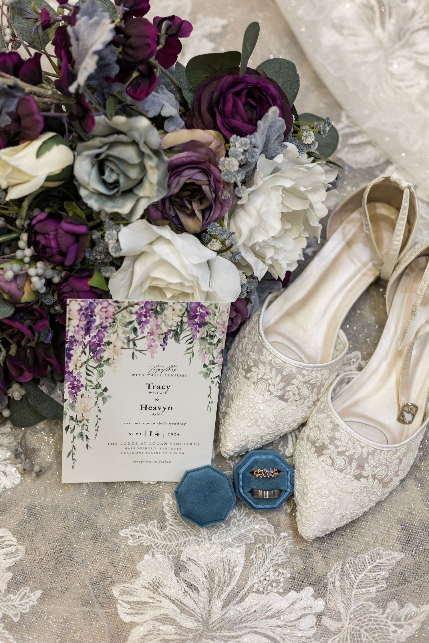 Wedding details flat lay with purple florals, lace shoes, and invitation featuring cascading wisteria design.