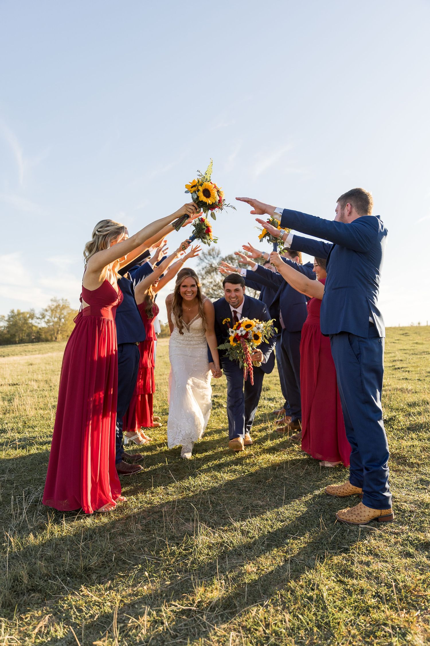 Wedding party creates an archway with sunflowers as couple walks beneath.