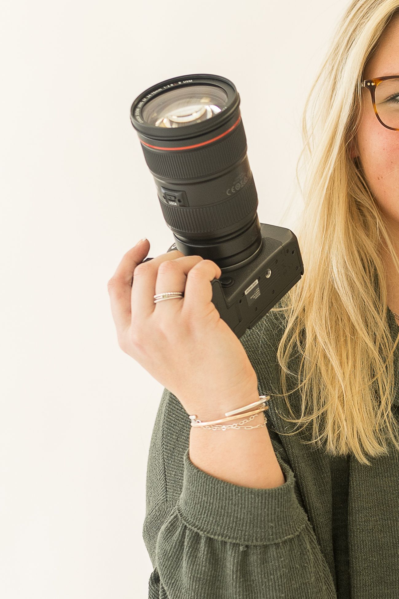 Close up of camera with telephoto lens held by photographer wearing green sweater.