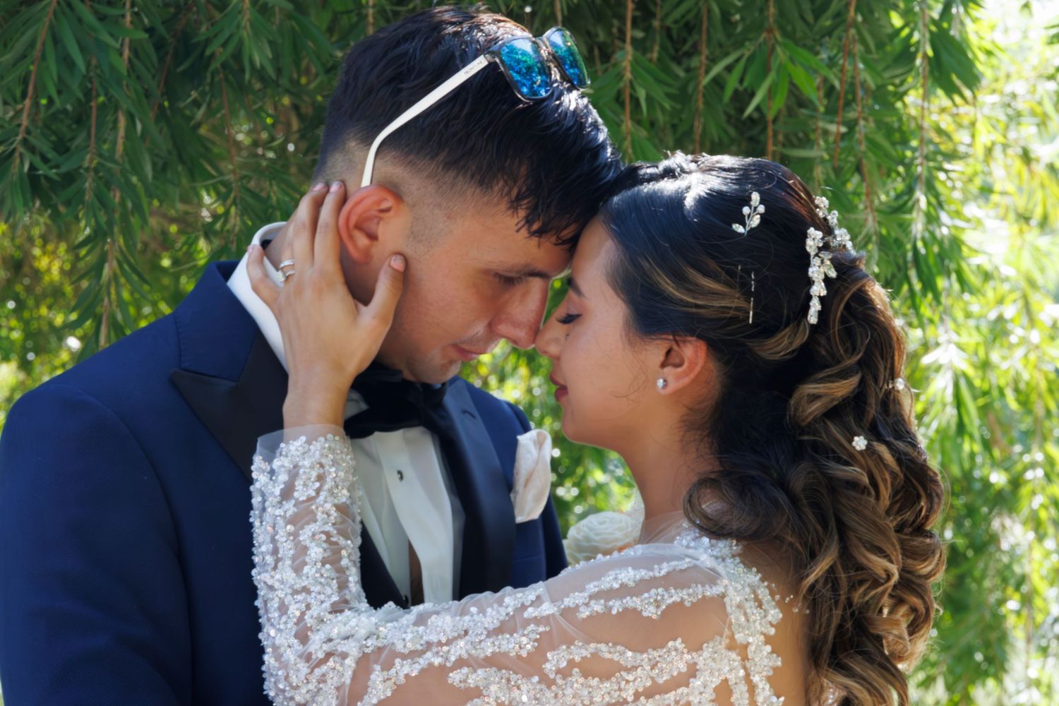 A romantic wedding couple shares intimate kisses in a garden setting with lush greenery in the background.
