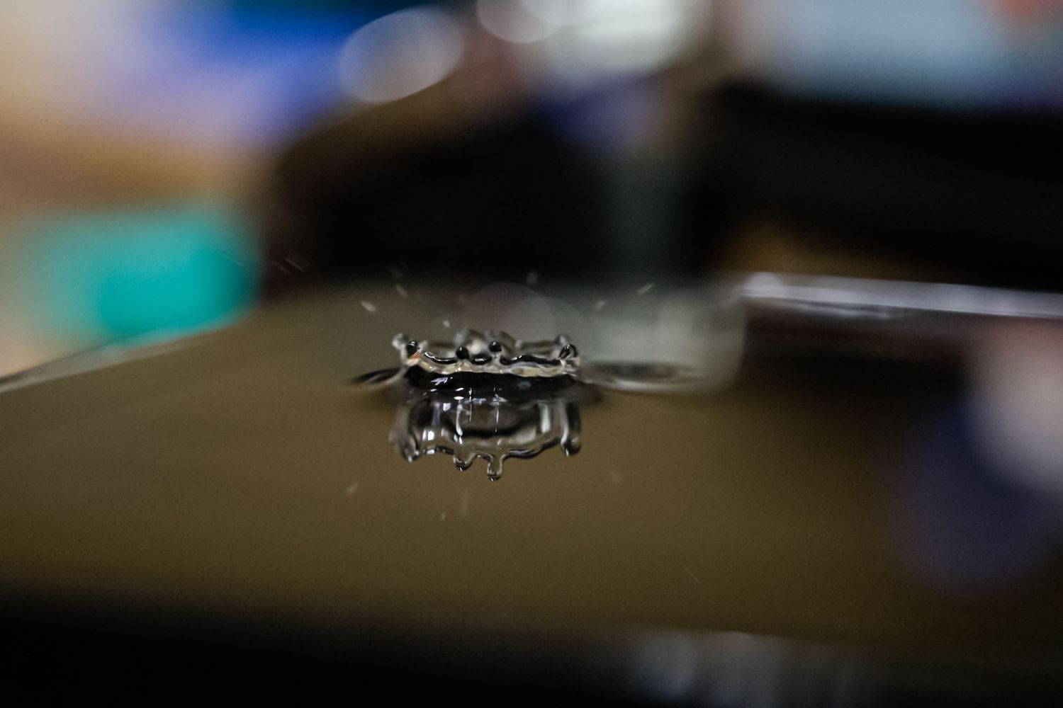 Close-up macro shot of a water droplet crown splash on a dark reflective surface with blurred background.
