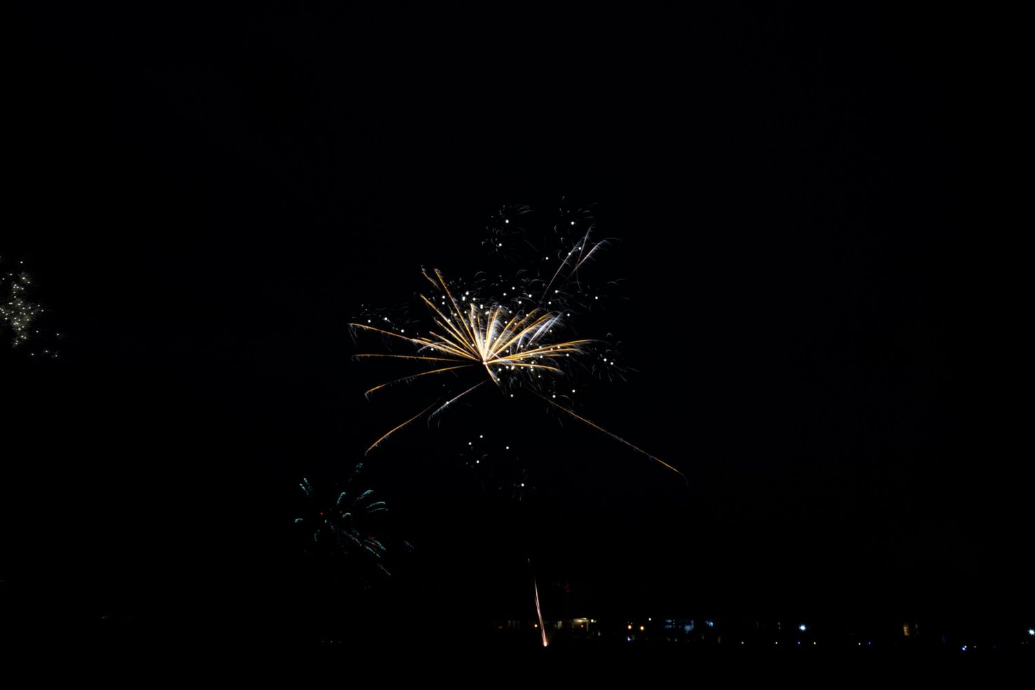 Fireworks burst in a dark night sky creating a white sparkly display against the black background.