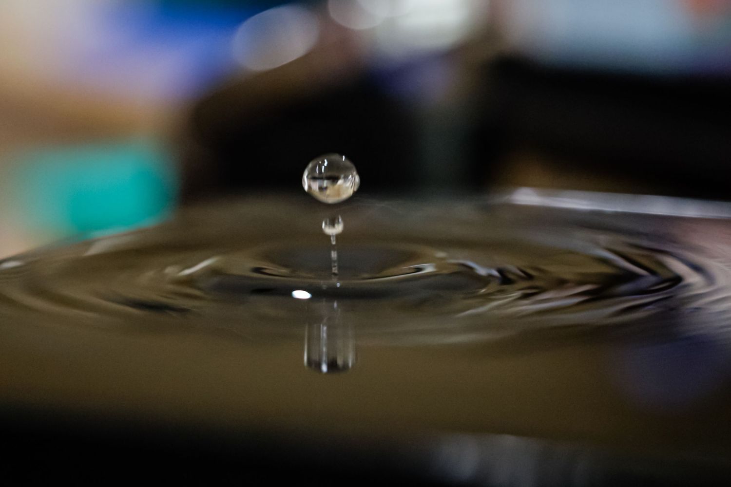 Close-up of a water droplet suspended above a rippling water surface, captured in stunning macro photography.