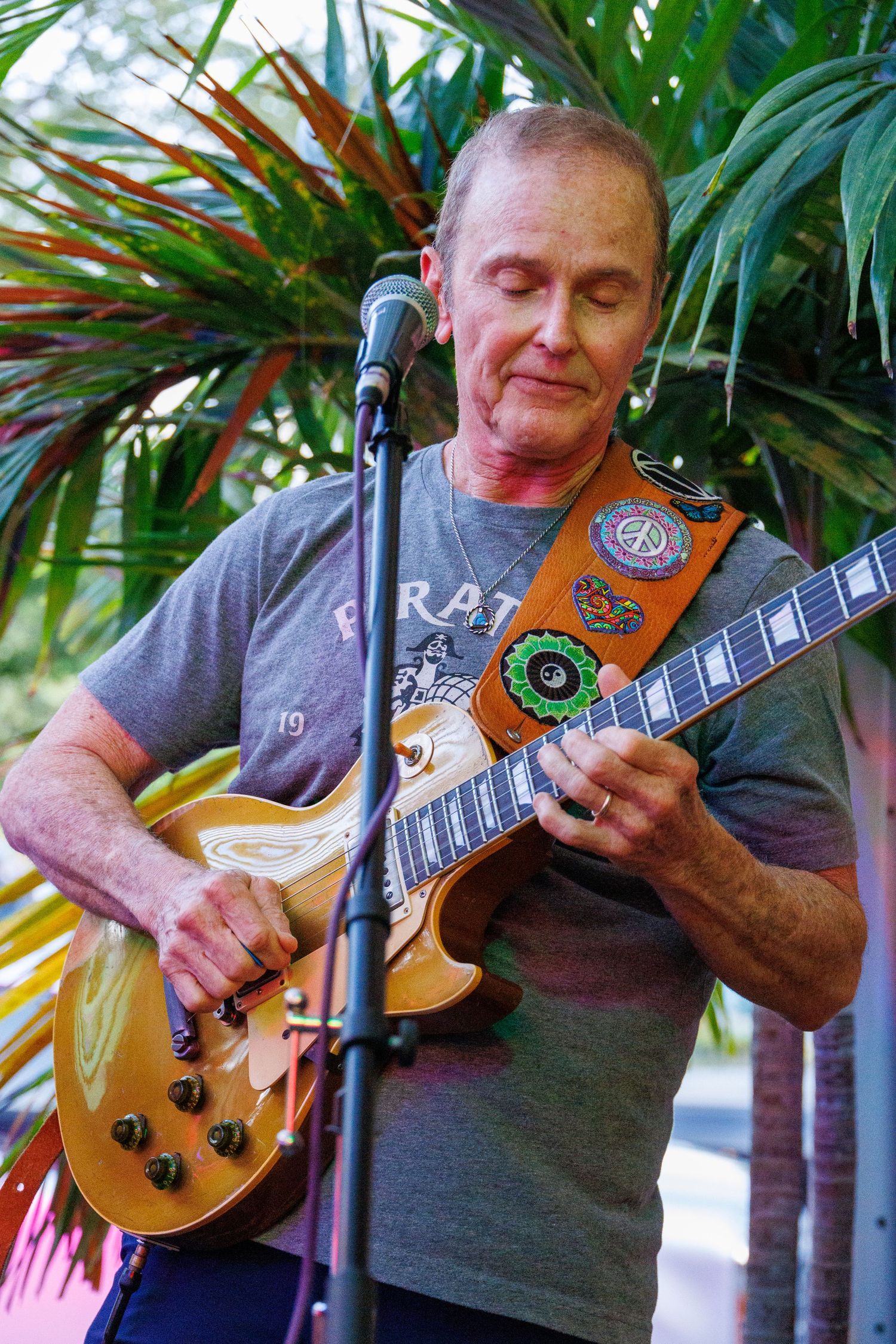 A musician plays a golden Les Paul guitar against a tropical palm background in a series of close-up shots.