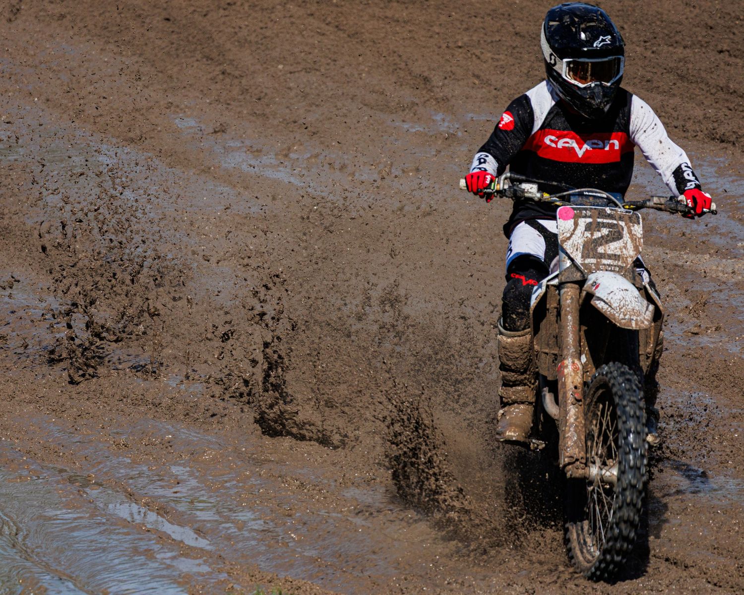Dirt bike rider splashing through muddy terrain during off-road motorcycle racing action.