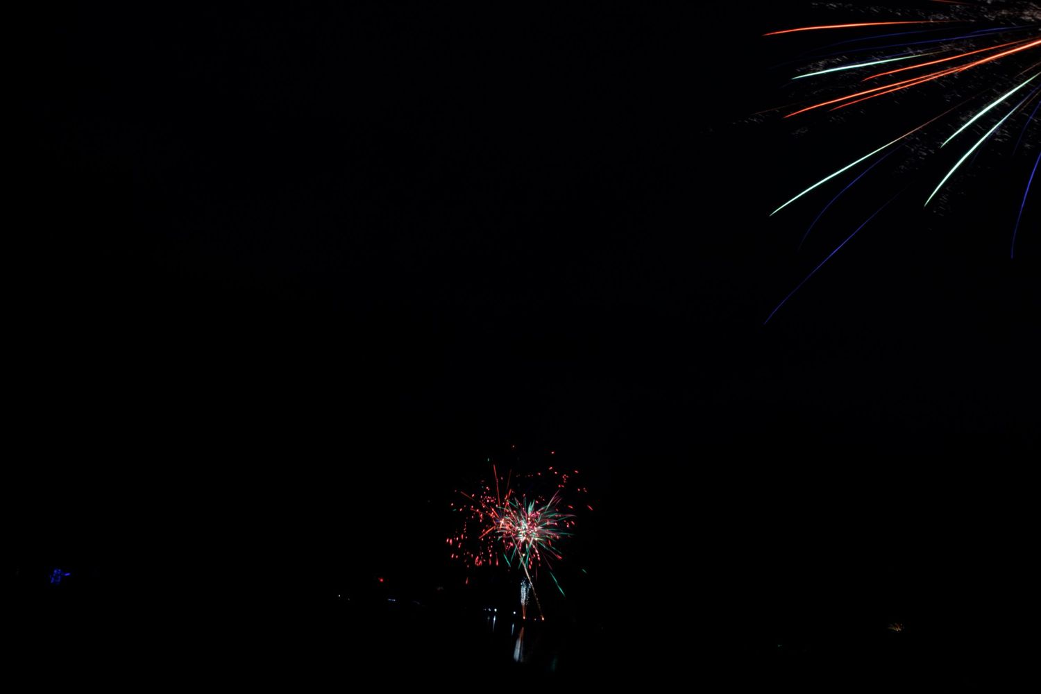 Fireworks explode in a dark night sky creating colorful bursts of red, white and blue light against the black background.