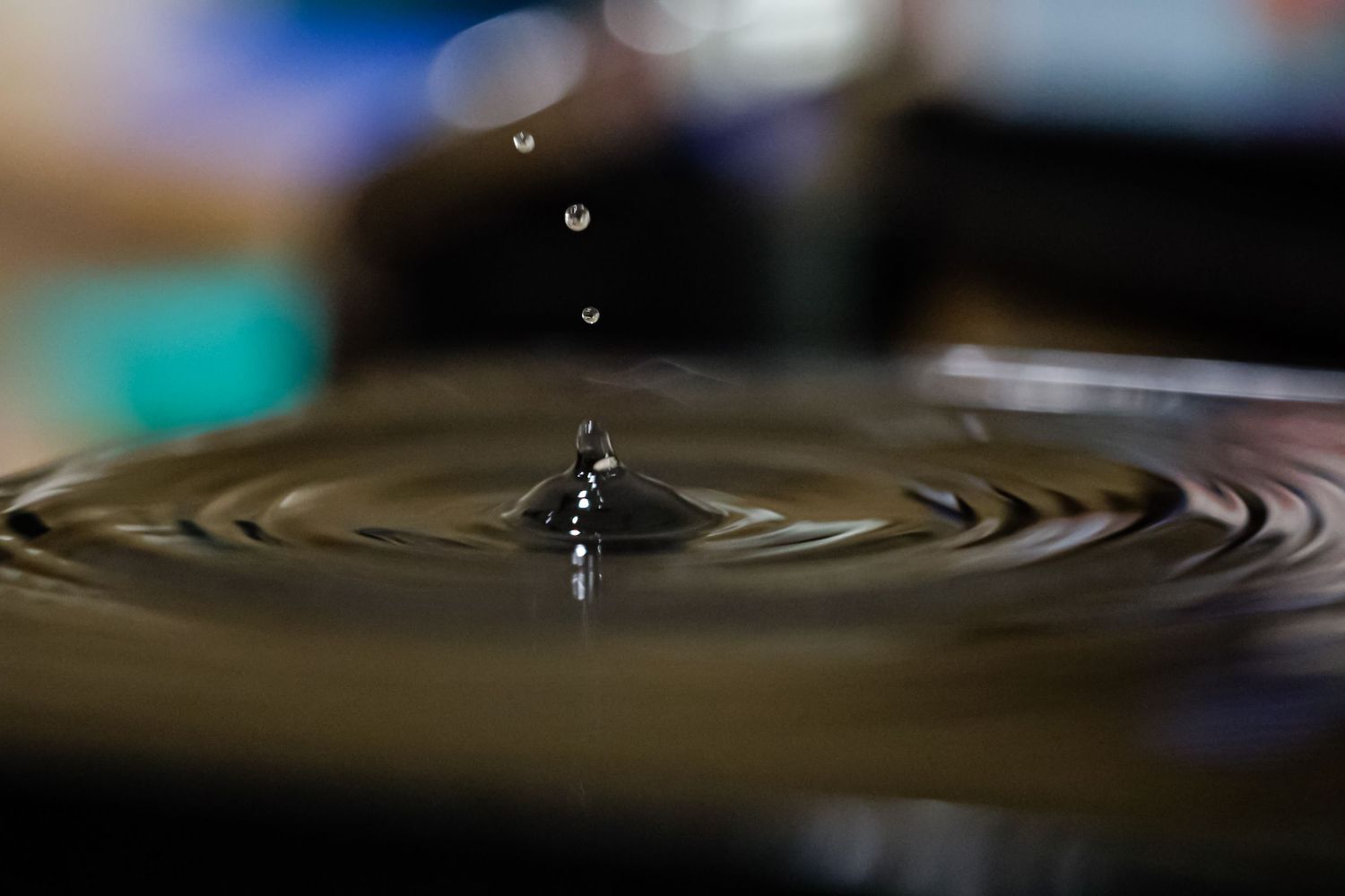 Close-up of a water droplet creating ripples on a dark water surface with bokeh background.