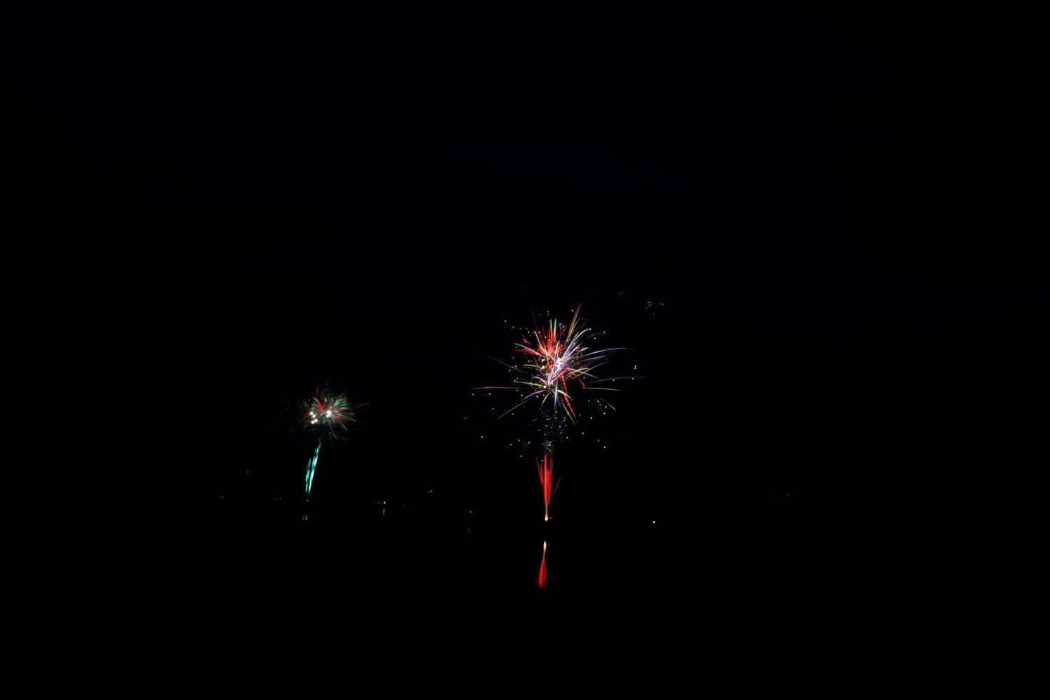 Colorful fireworks bursting against a dark night sky with red and white sparks trailing downward.