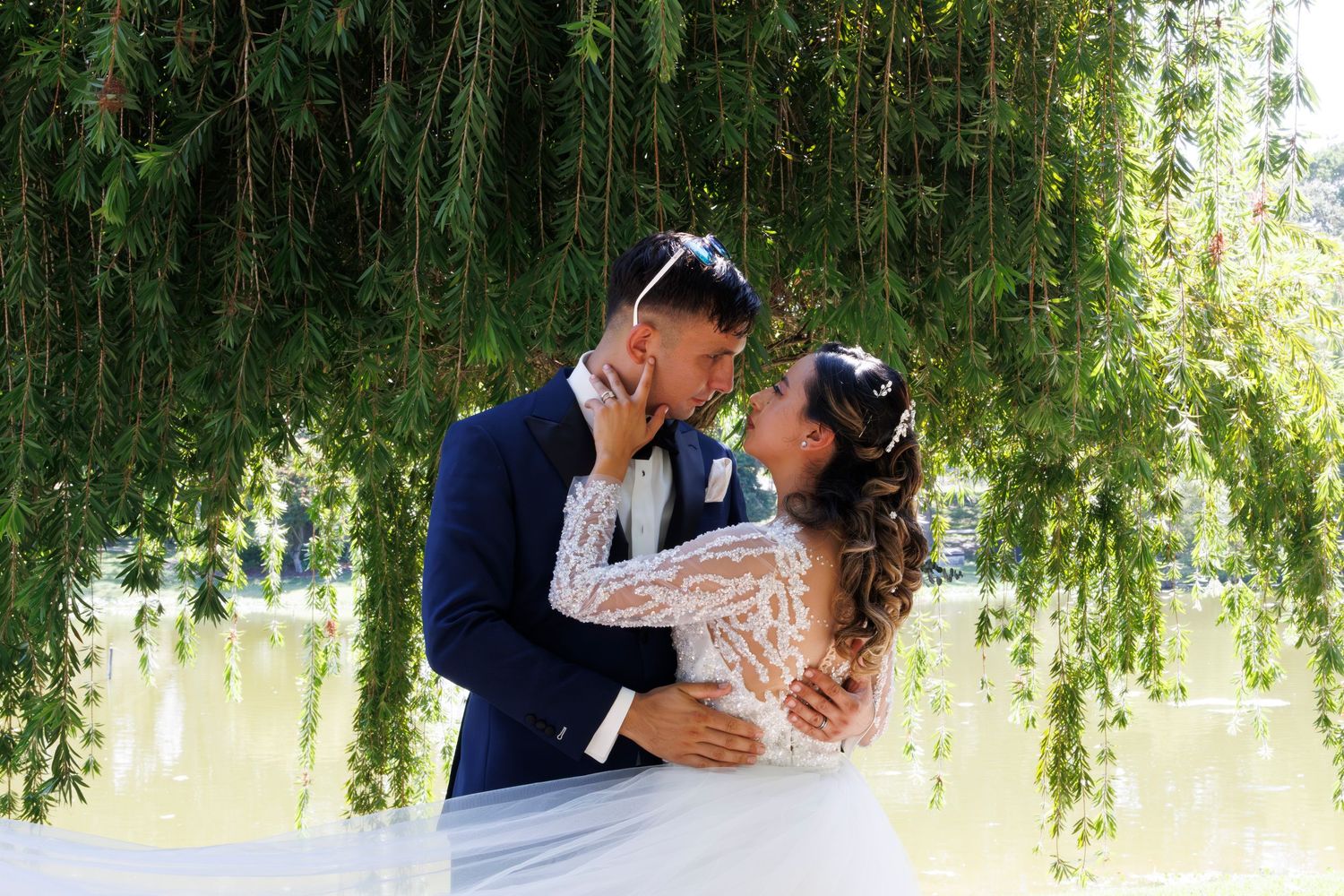A couple shares a romantic kiss under a weeping willow tree during their wedding photoshoot.