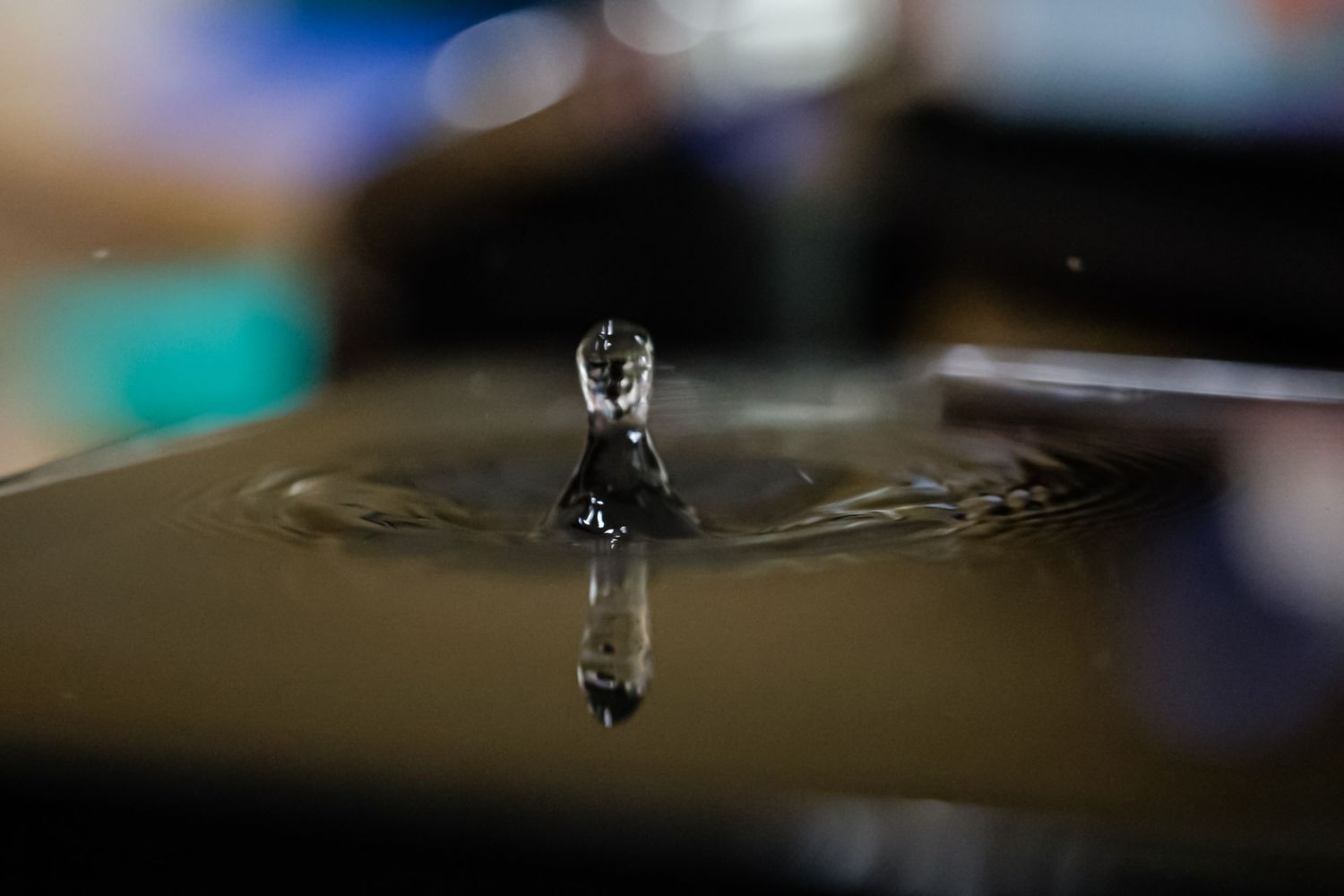 Close-up macro shot of a water droplet forming a crown splash on a dark reflective surface.