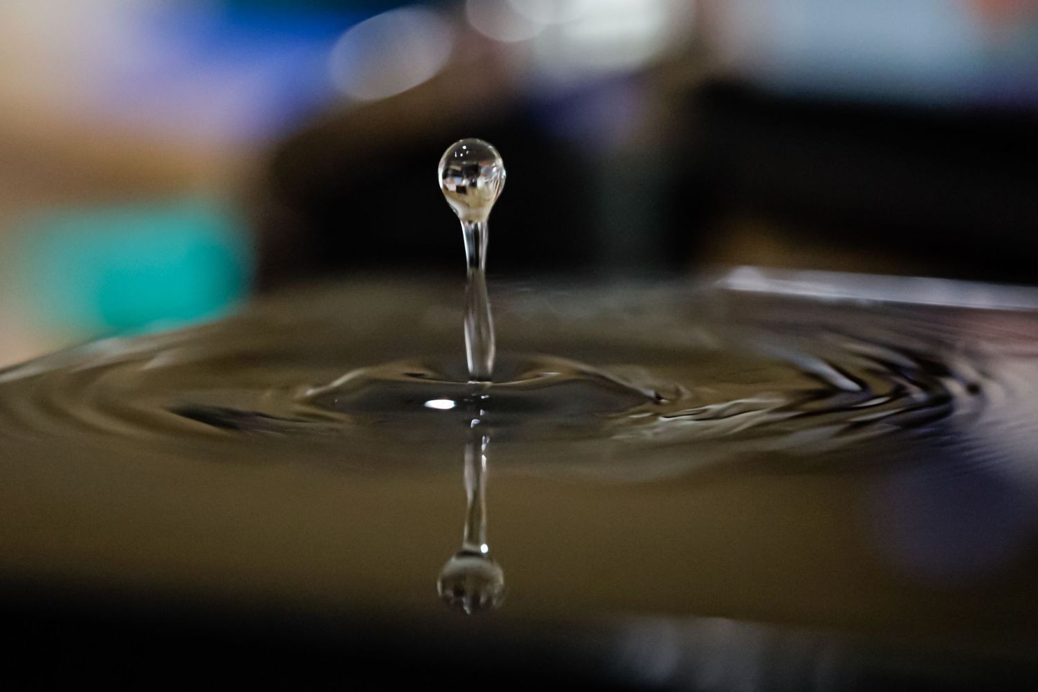 A stunning macro shot of a water droplet suspended mid-air above a rippling water surface with a dark background.