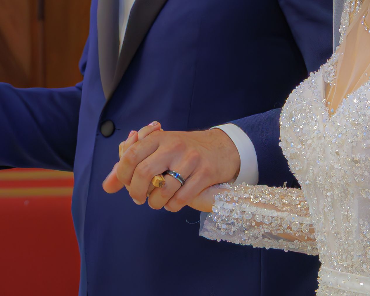 Close up of hands exchanging wedding rings during a ceremony with bride in white lace dress and groom in navy suit.