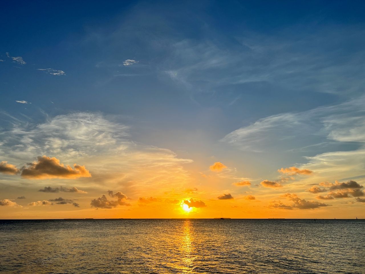Vibrant orange sunset over calm ocean waters with scattered clouds and golden reflections on the horizon.