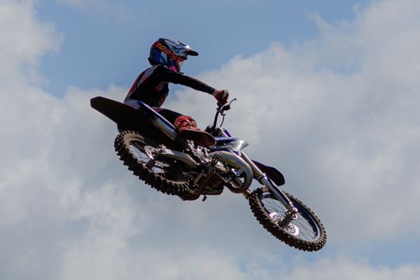 A sequence of motocross bike jumps showing a rider performing aerial tricks against a cloudy sky background.