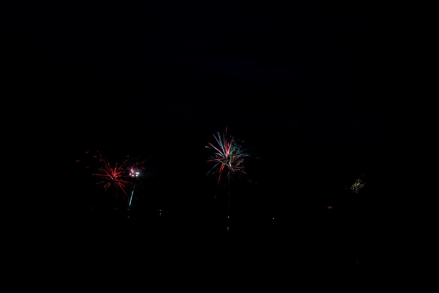 Colorful fireworks burst against a dark night sky in multiple bright explosions of red, blue and white light.