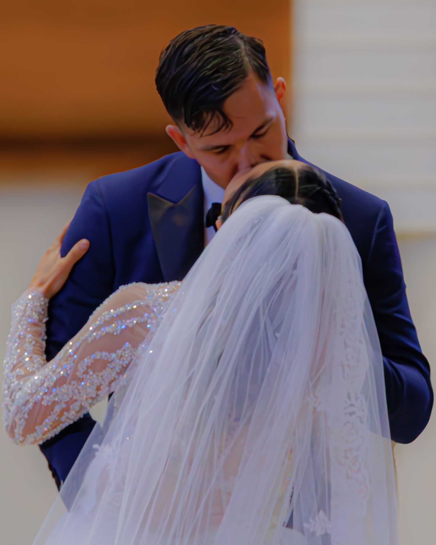A couple in wedding attire share an intimate kiss under a flowing white veil.
