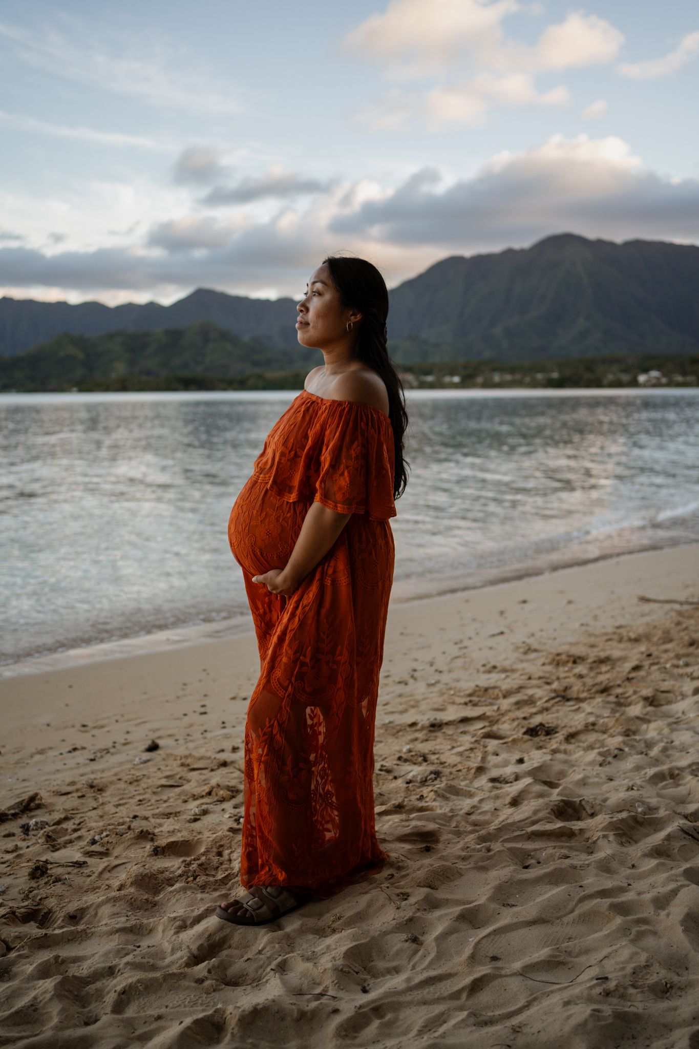 Person in orange dress standing on beach with mountains in background.