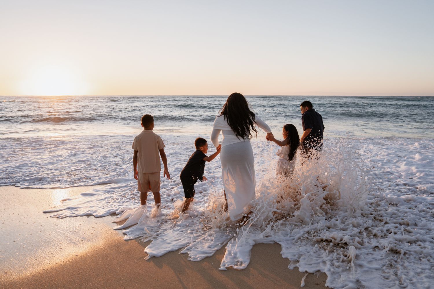 Family splashing in ocean waves during sunset beach photoshoot.