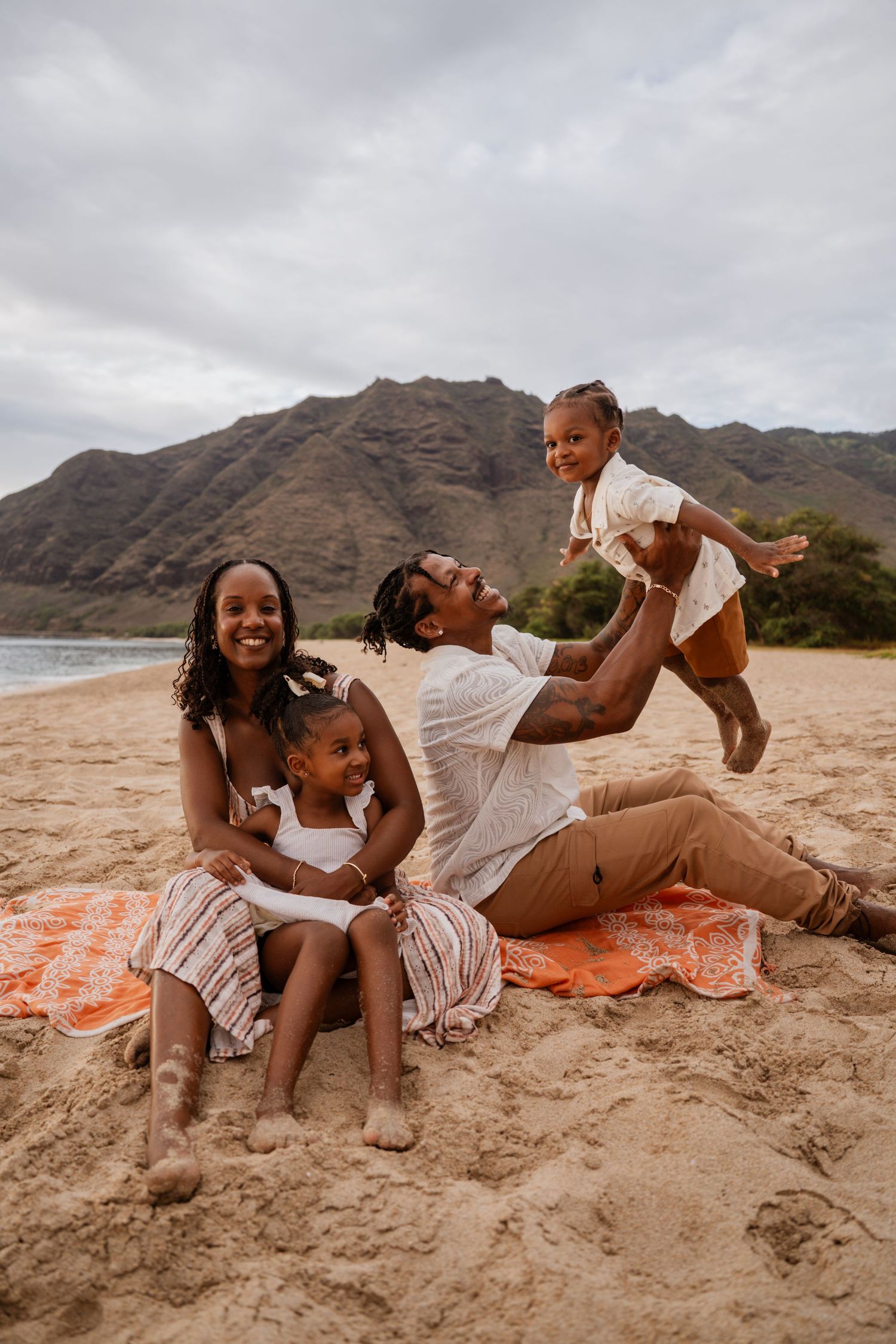 A couple relaxes together on a beach blanket with mountains in the background near the ocean.