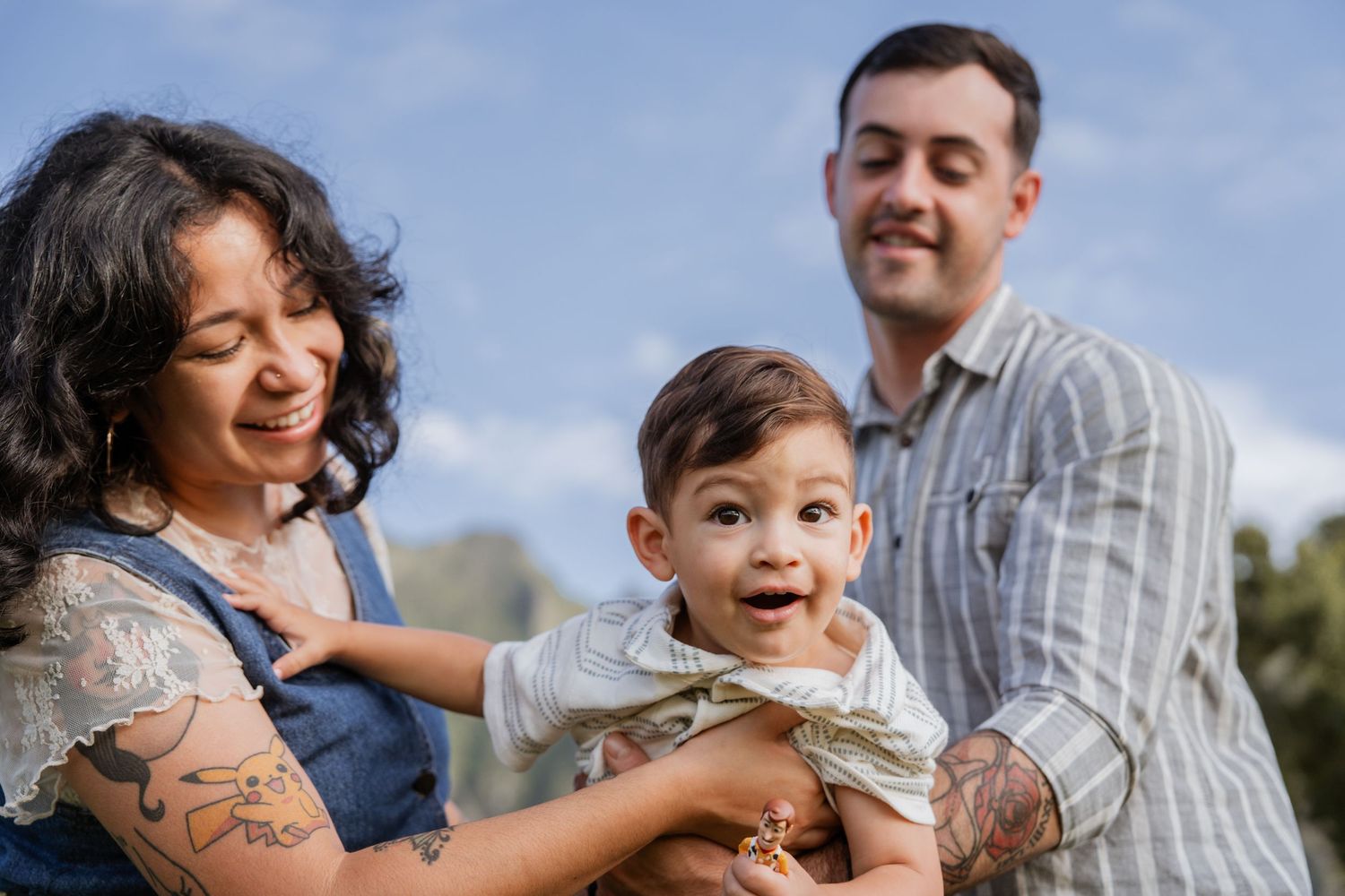 A cheerful family of three enjoying an outdoor moment together against a blue sky backdrop.