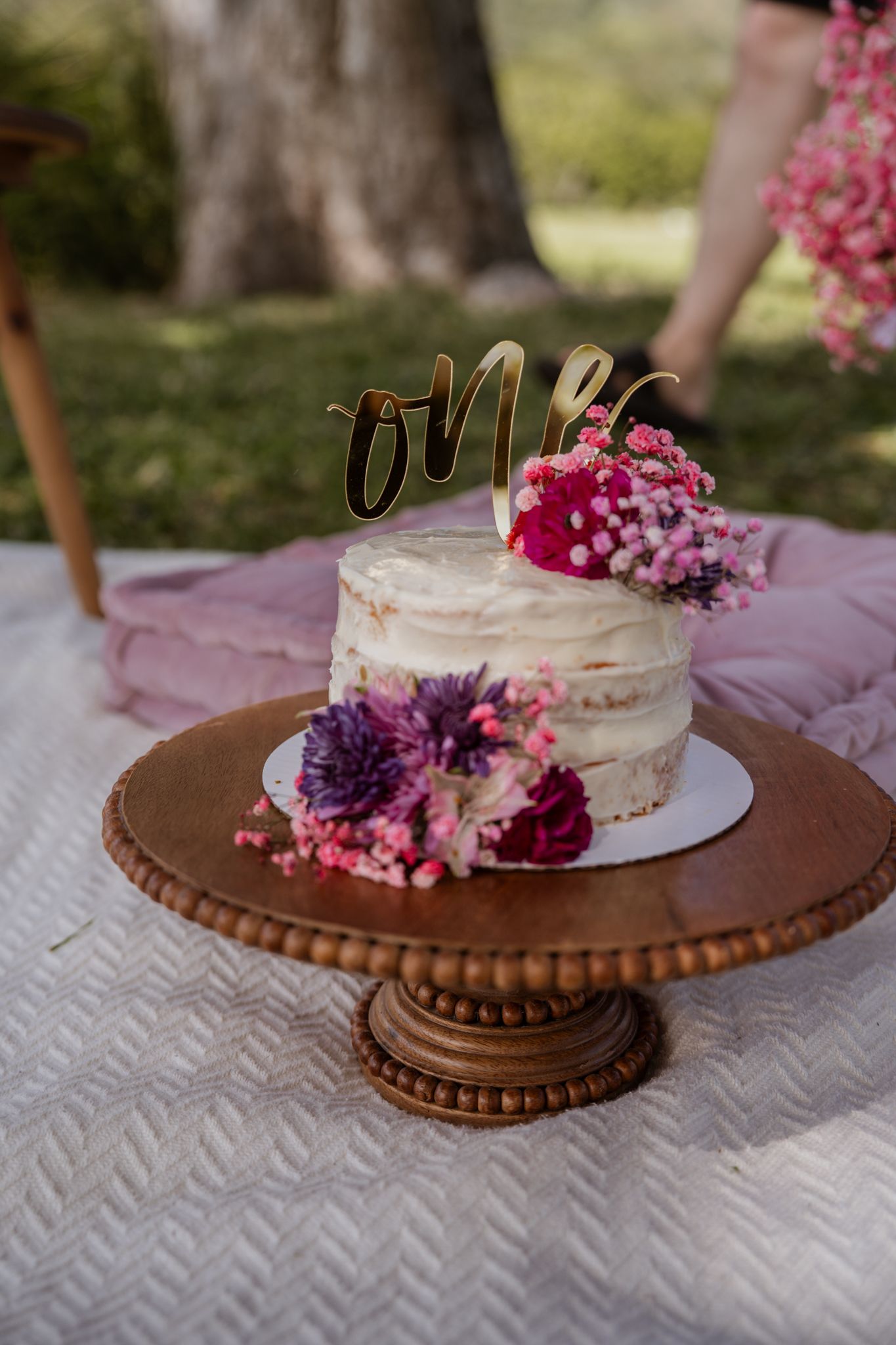 Rustic wedding cake decorated with pink and purple flowers on ornate copper pedestal.