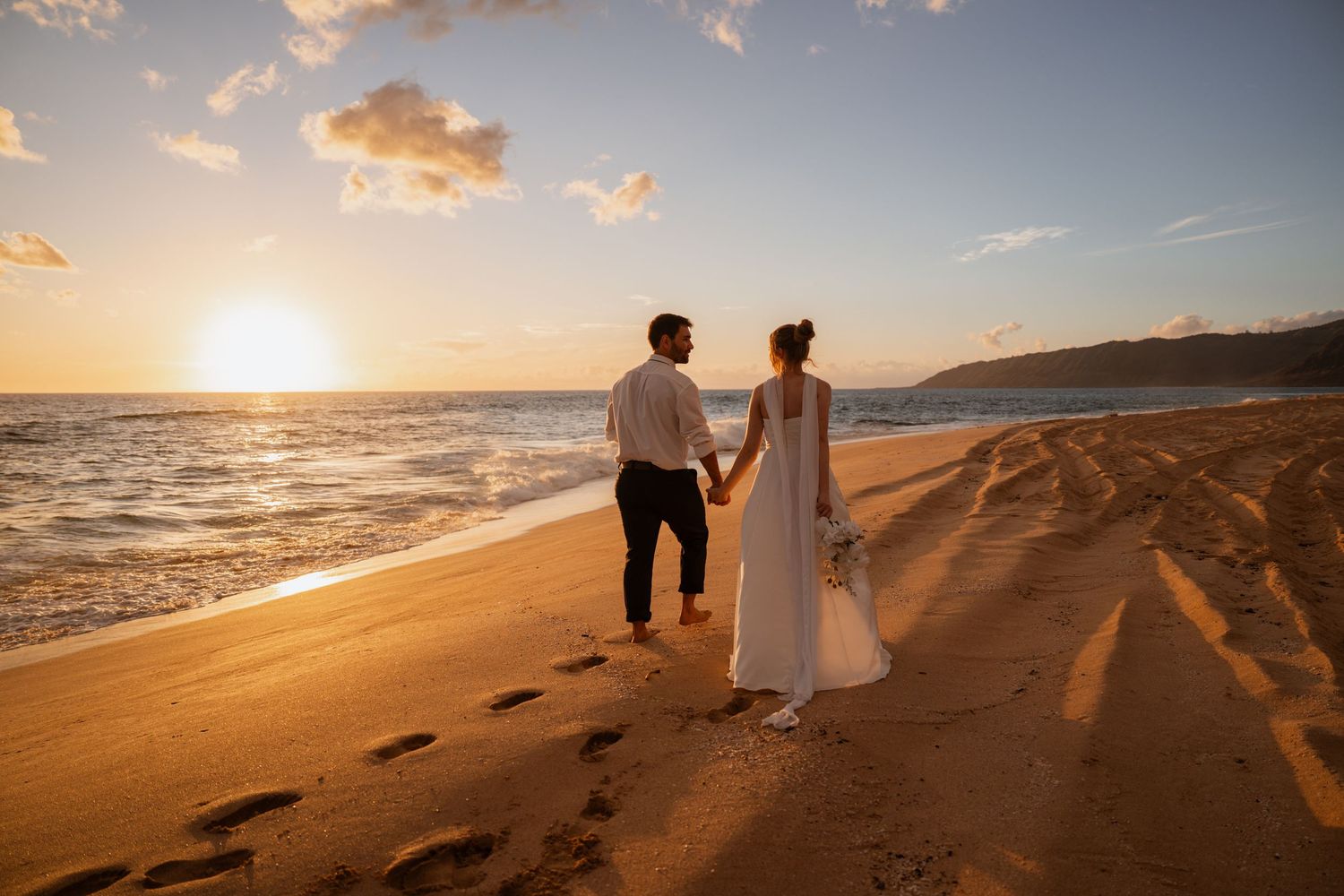 Romantic sunset beach photoshoot with couple walking along sandy shore casting long shadows at golden hour.