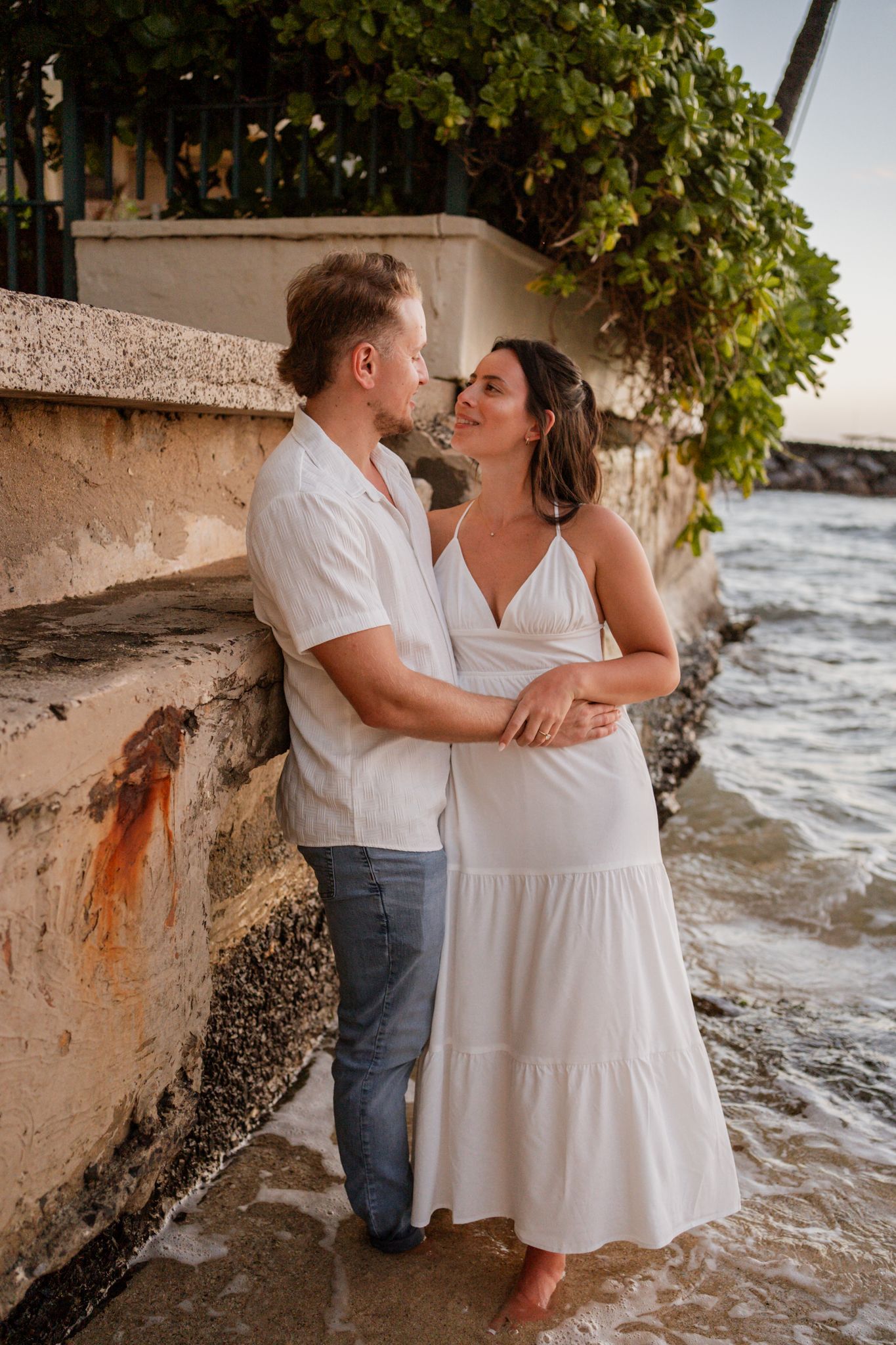 Couple sharing intimate moment against coastal wall at sunset.