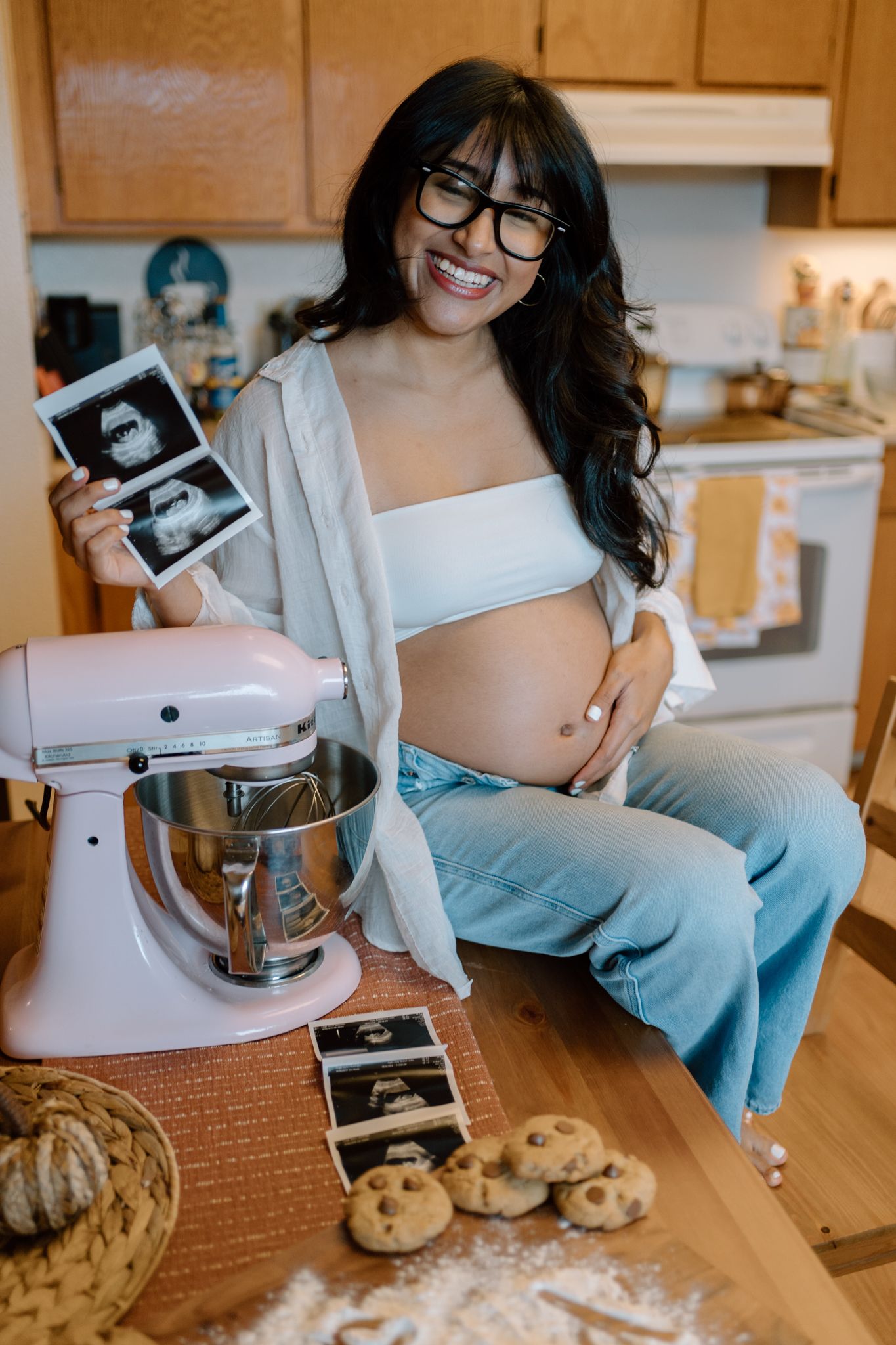 Expecting person in kitchen holding ultrasound photos next to stand mixer and cookies.
