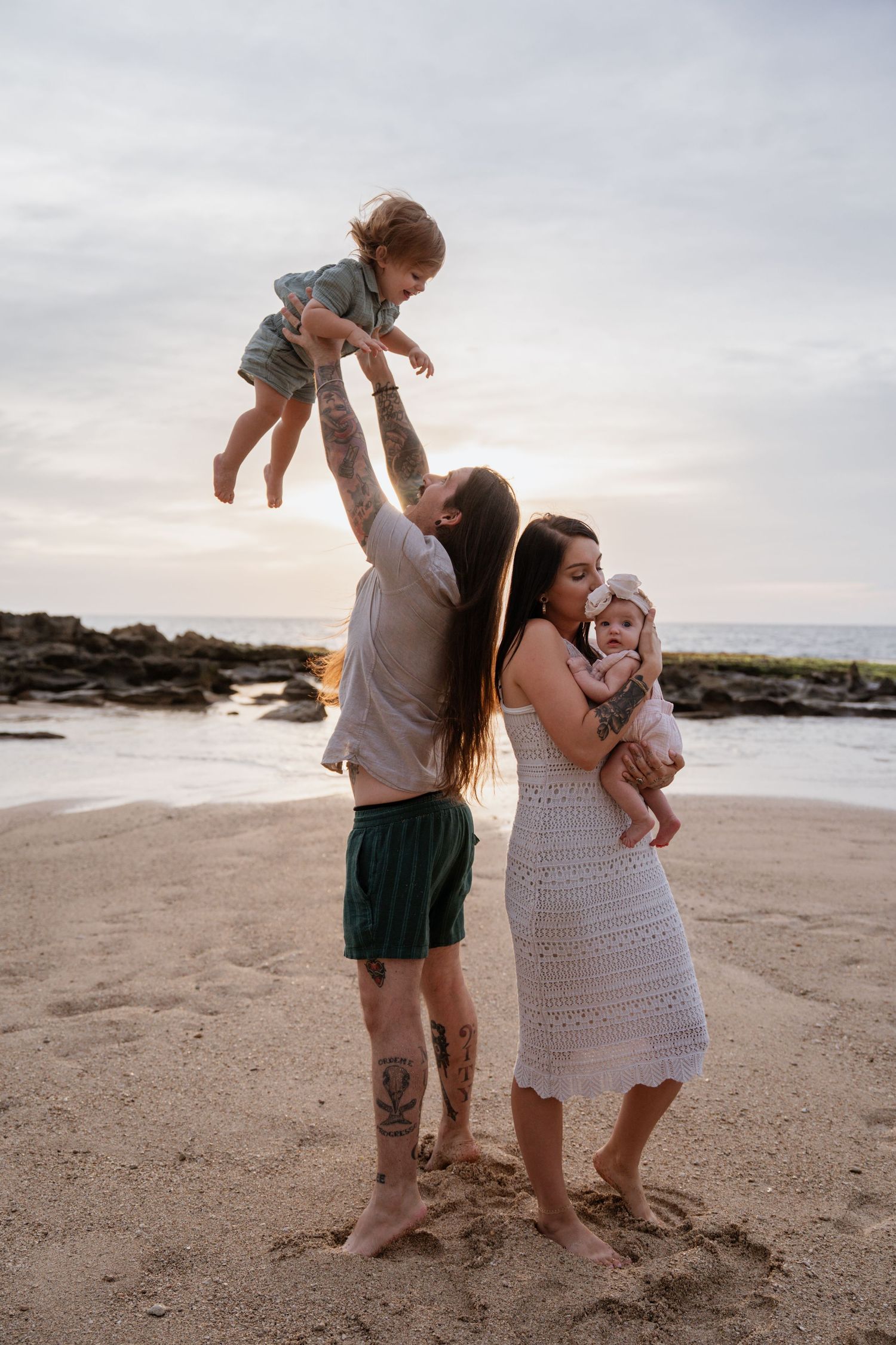 A family shares playful moments together on a sandy beach at sunset, creating joyful memories by the ocean.